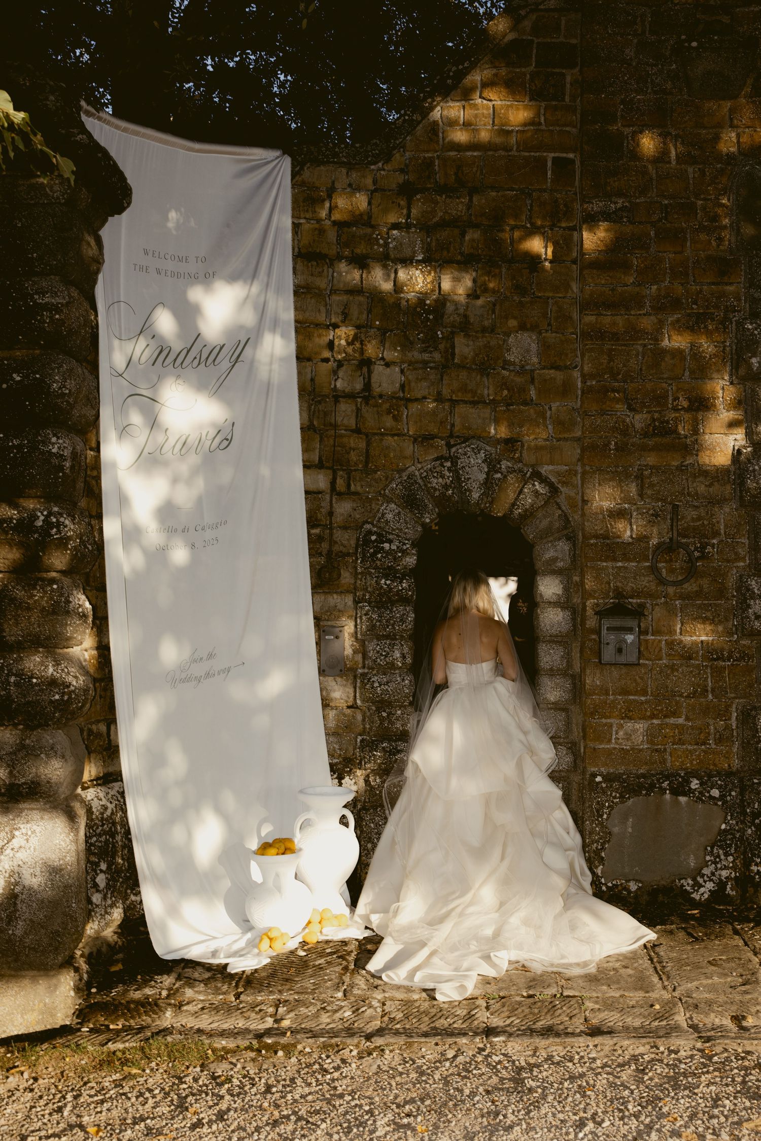 A series of white wedding dresses displayed against a rustic brick wall with dappled lighting creating a romantic ambiance.
