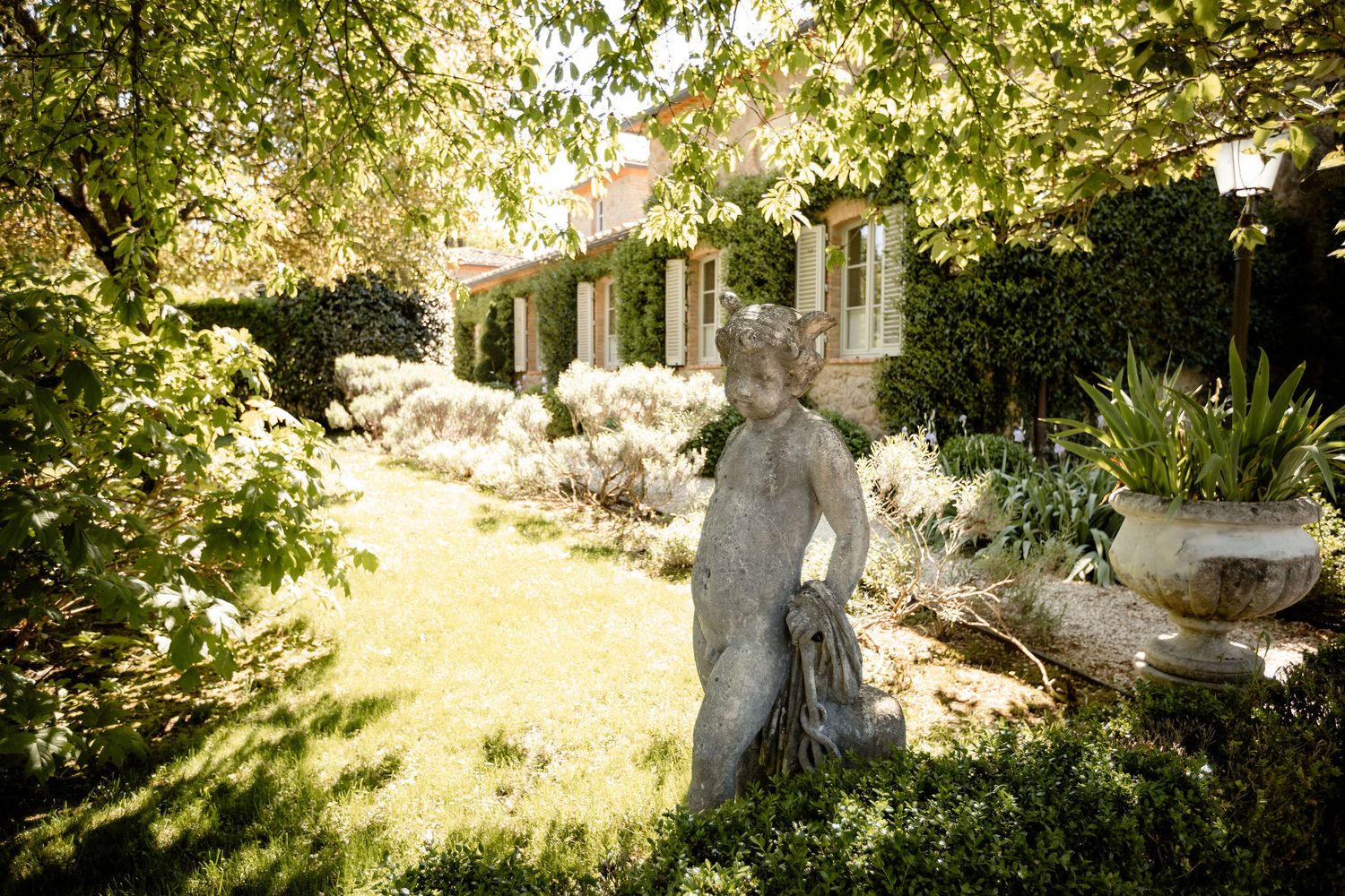 A charming garden patio with a stone statue among blooming white flowers and dappled sunlight through lush foliage.