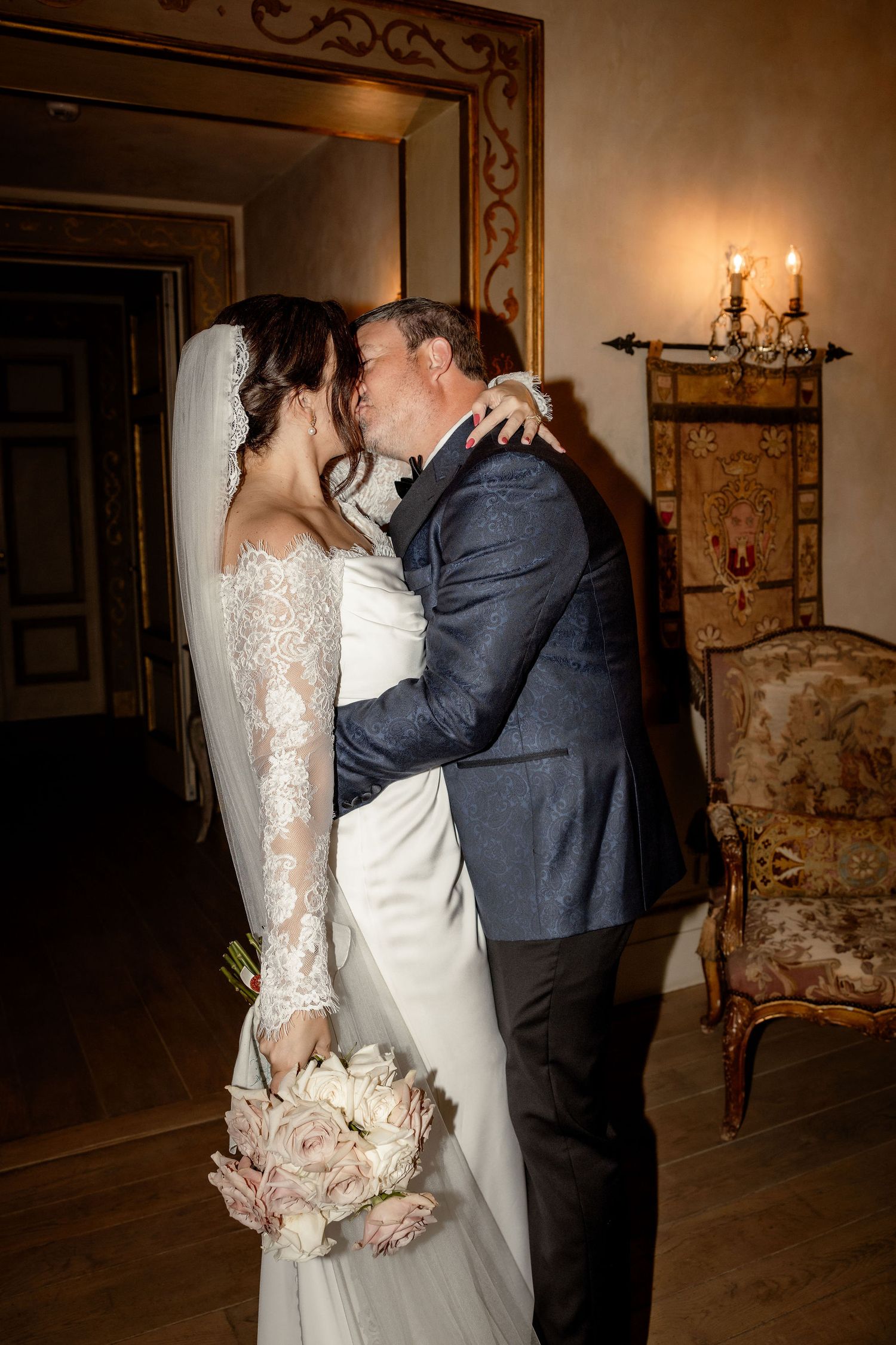 Newlywed couple shares an intimate moment in an elegant indoor setting with vintage furnishings and warm lighting.