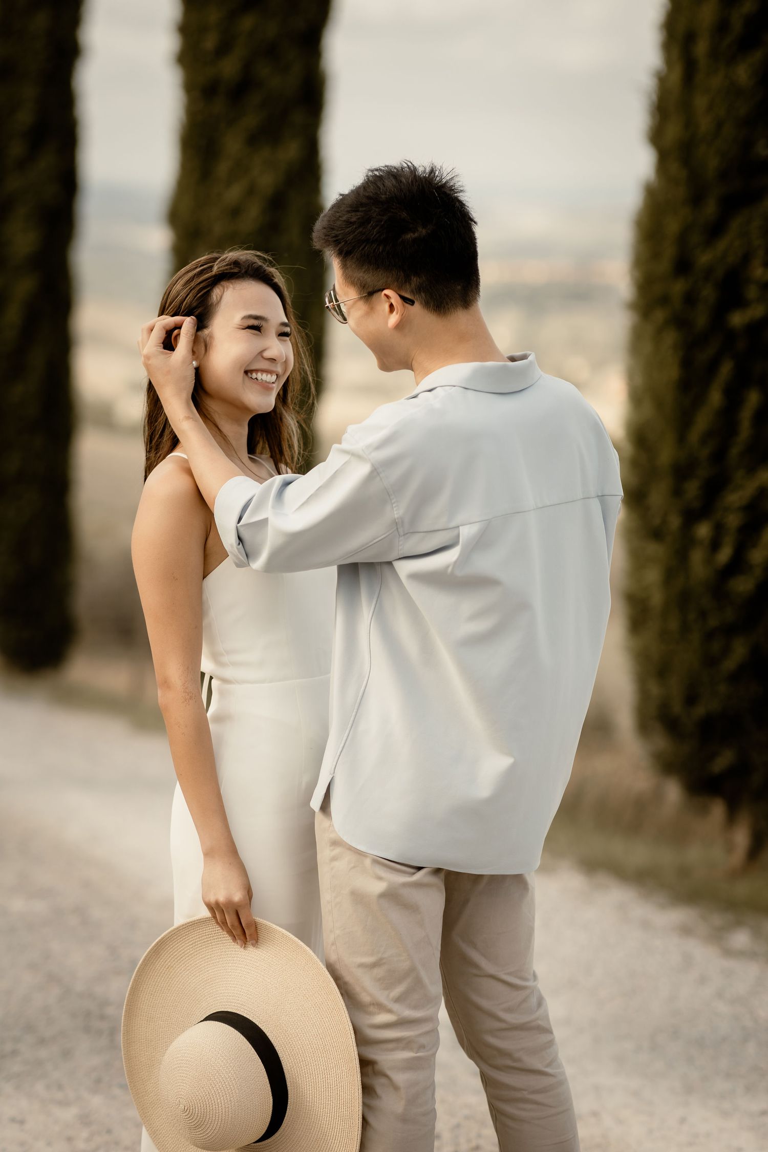 Intimate moment between couple on rural road with tall cypress trees in Italy.
