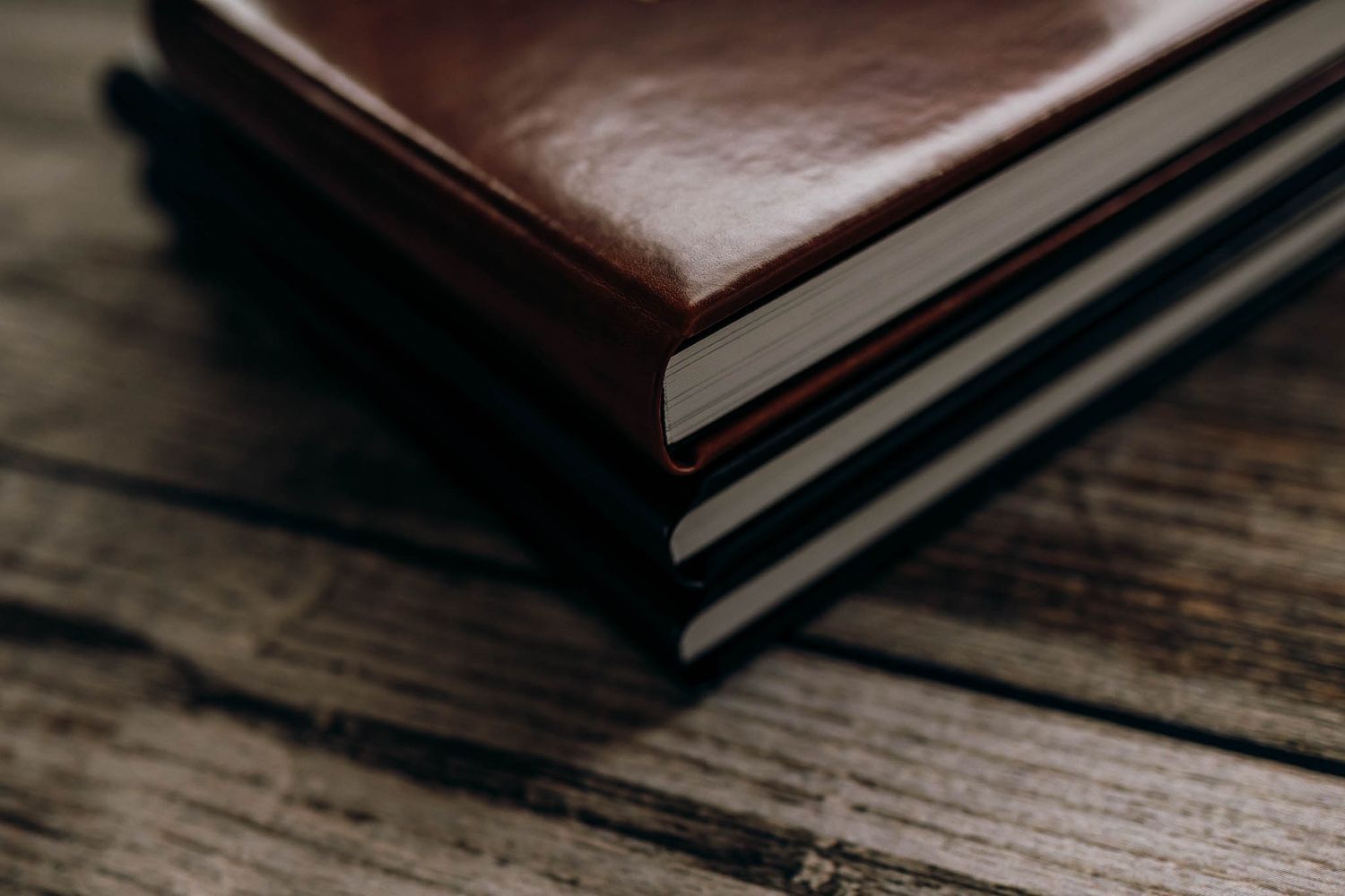 Stack of brown leather notebooks sitting on rustic wooden table in shallow depth of field.