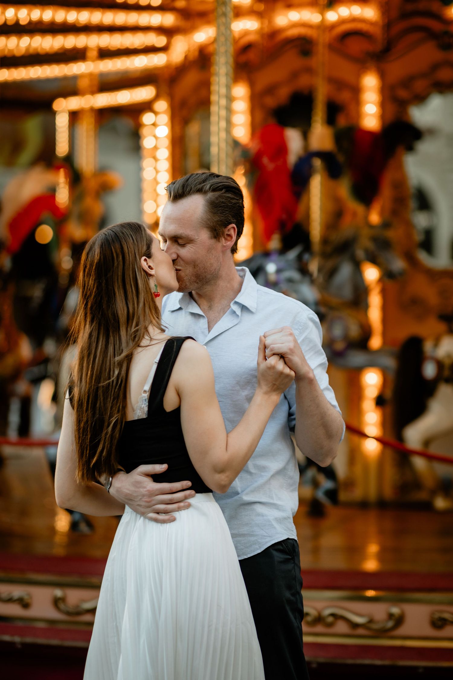 A romantic couple dancing near an illuminated vintage carousel at dusk.
