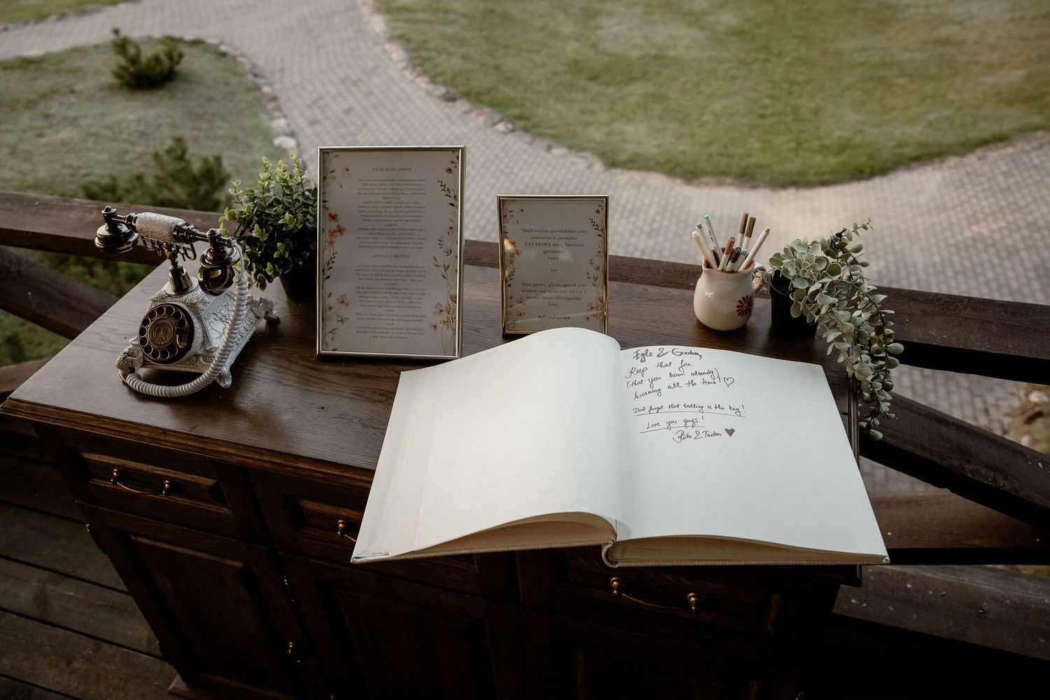An open guest book with a vintage camera and wildflower decorations on a rustic wooden table.