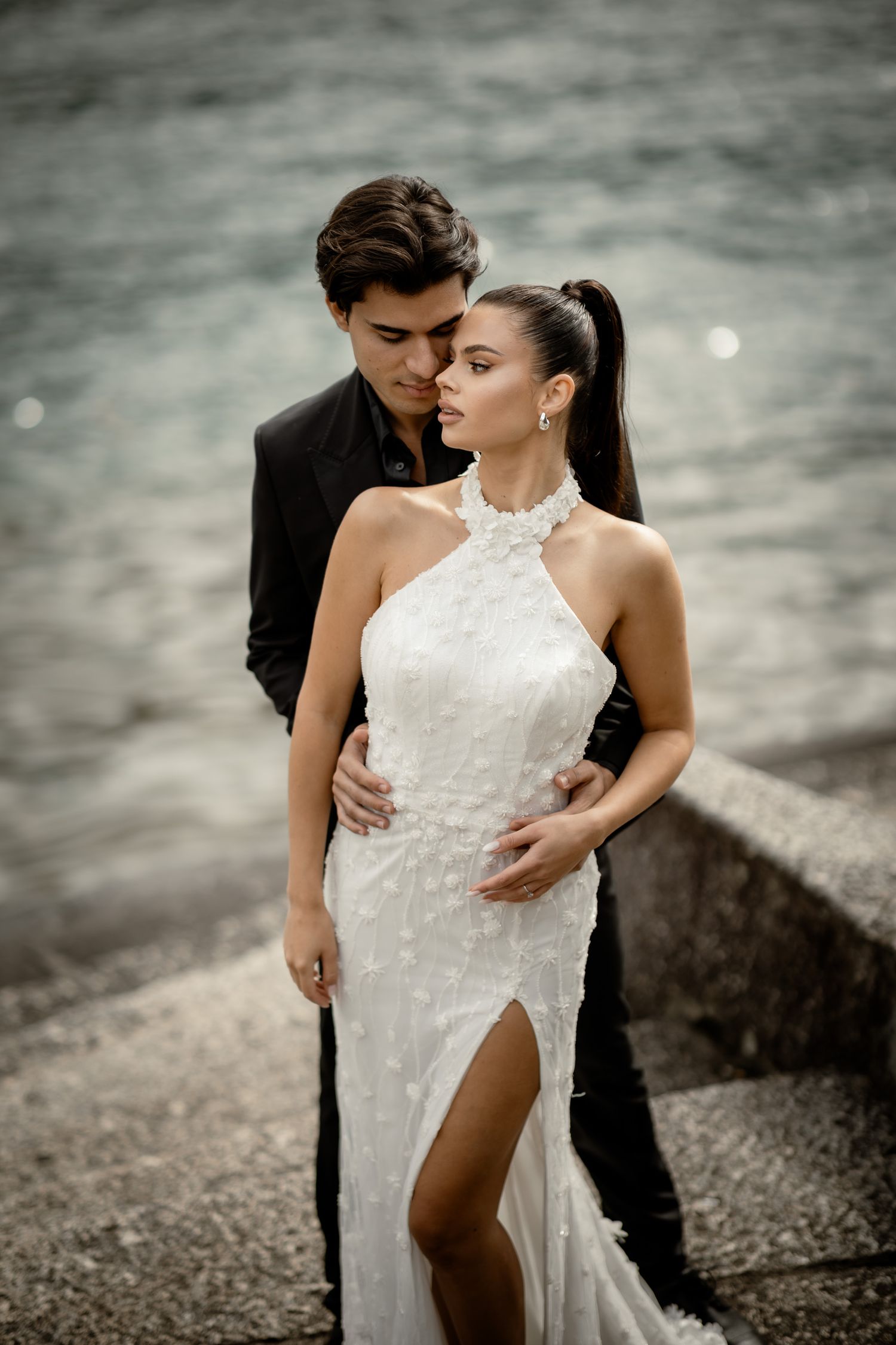 Romantic wedding portrait featuring elegant white halter dress against moody waterfront.