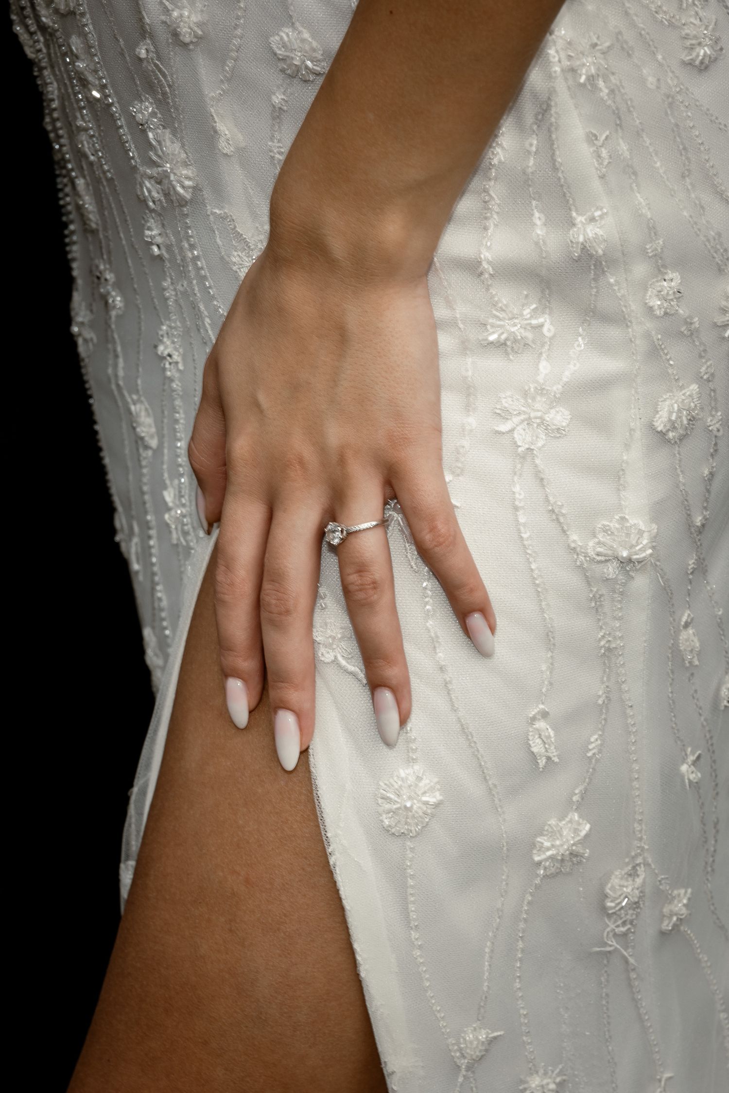 Close-up of bride's hand with wedding ring against detailed white lace dress.