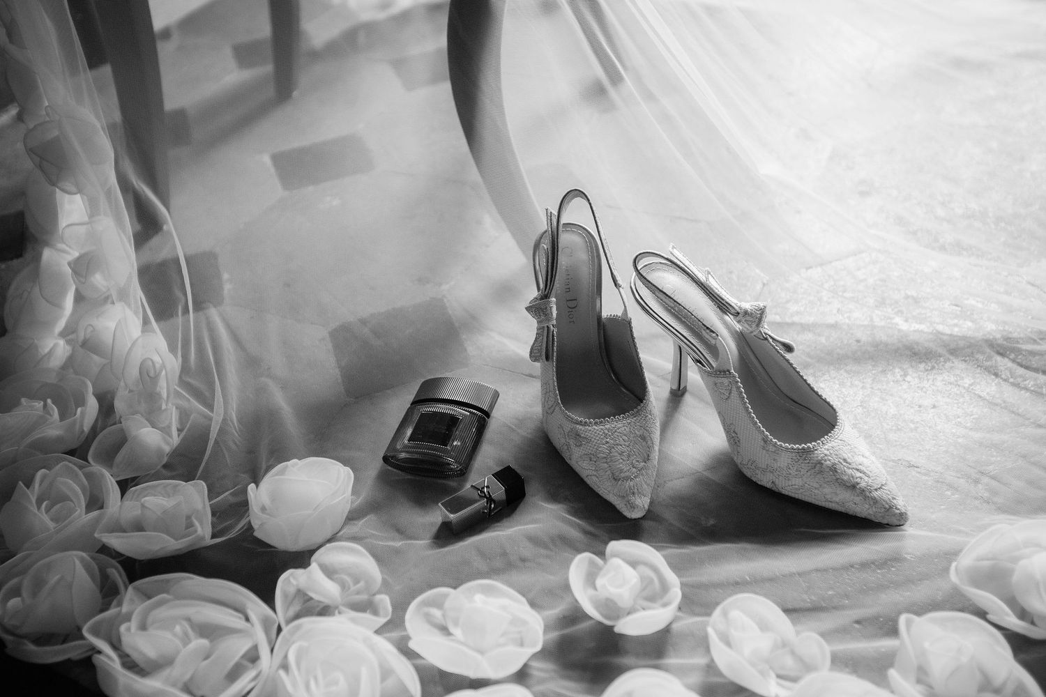 Black and white photo of elegant high heel shoes, cell phone and scattered roses creating a dreamy composition.