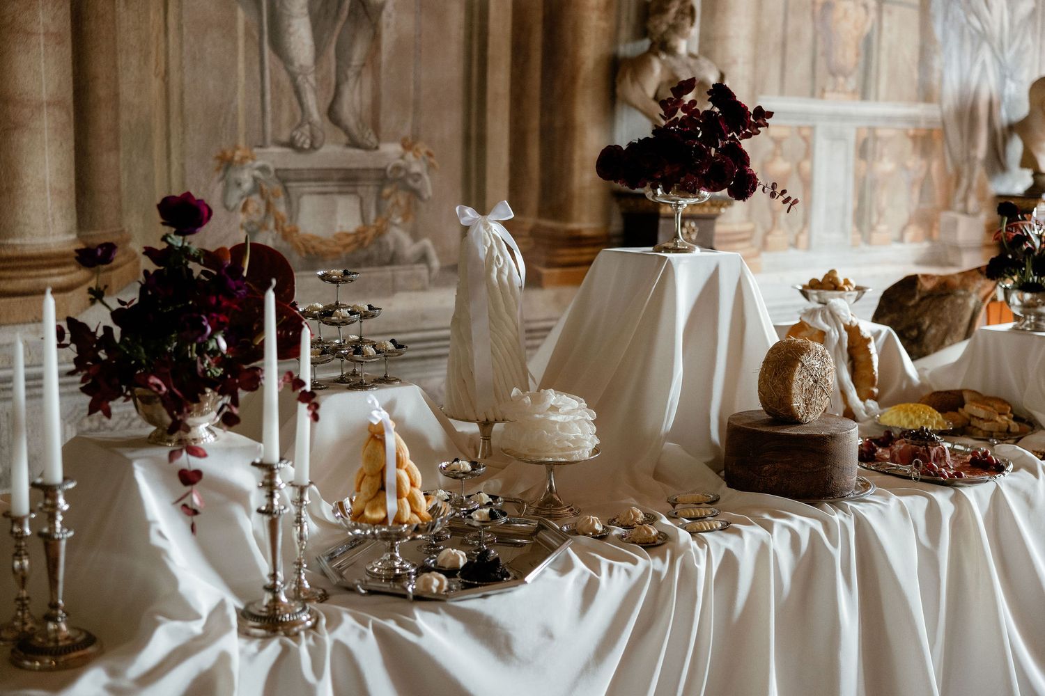 Elegant wedding reception display with white tablecloths, dark floral arrangements and ornate candelabras in a historic venue.