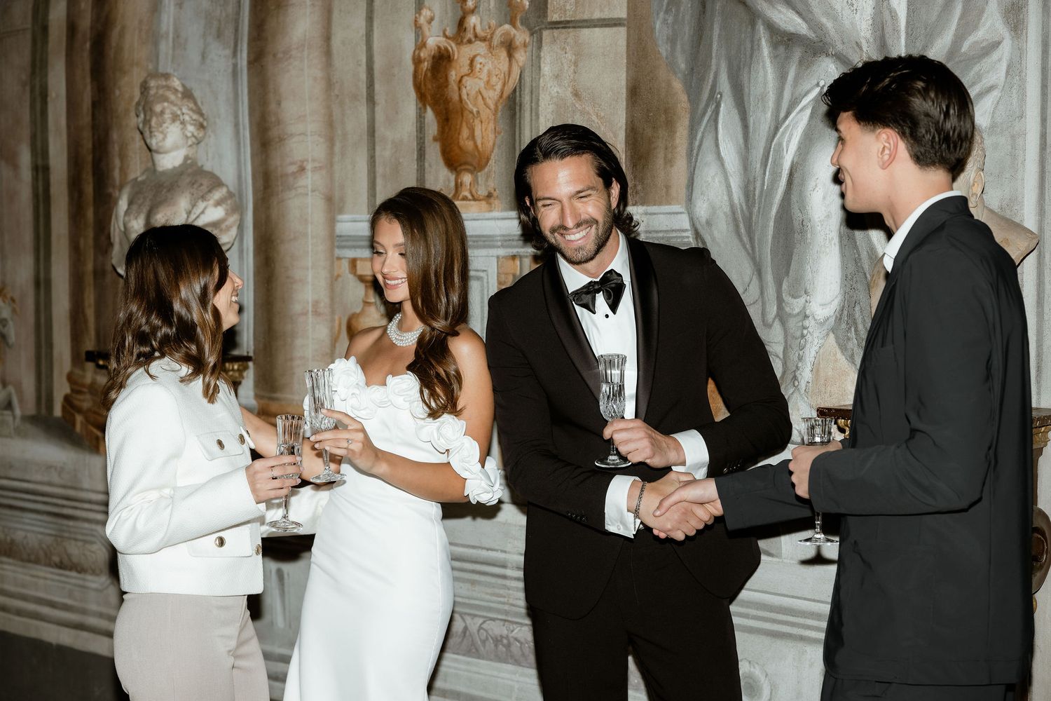 A group of elegantly dressed people wearing formal attire share drinks and conversation at an upscale event.
