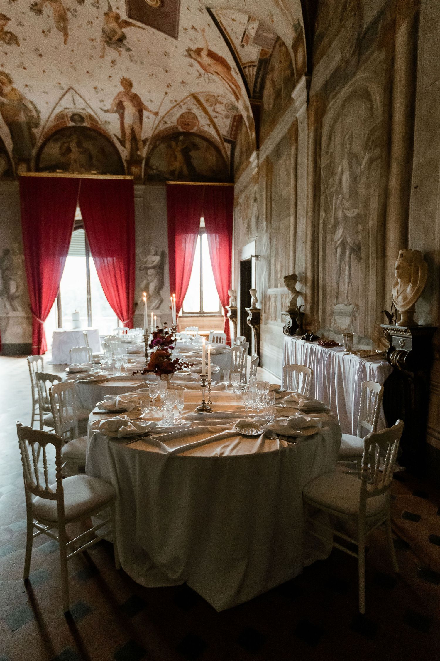 Elegant dining table set in vintage room with frescoed ceiling, red curtains and ornate decor at historic Italian villa.