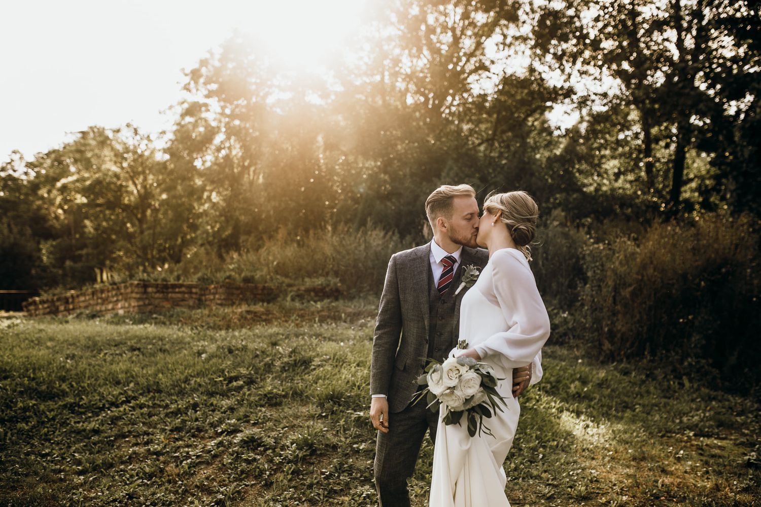 Romantic couple embraces in golden sunlight during outdoor wedding photo session at sunset.