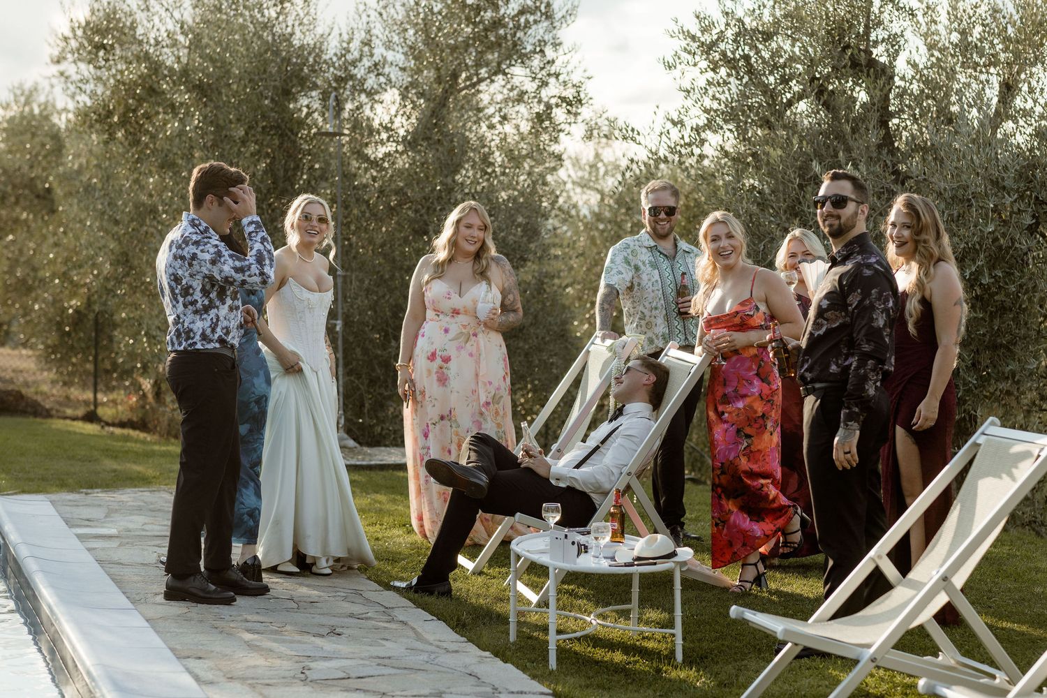 A group gathers for an outdoor celebration on a sunny evening among olive trees.