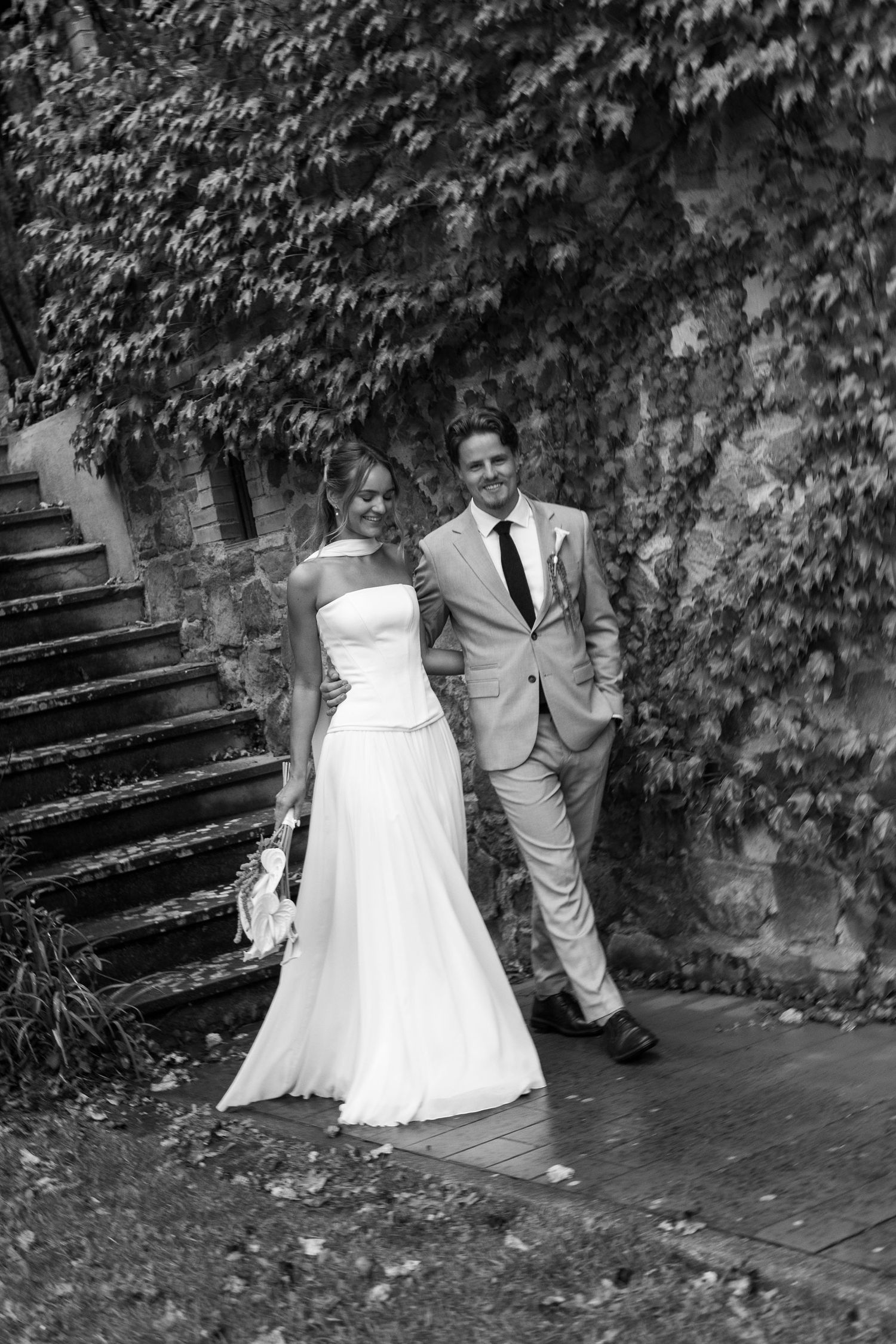 A romantic black and white wedding photo series showing a couple posing on stone steps surrounded by ivy.