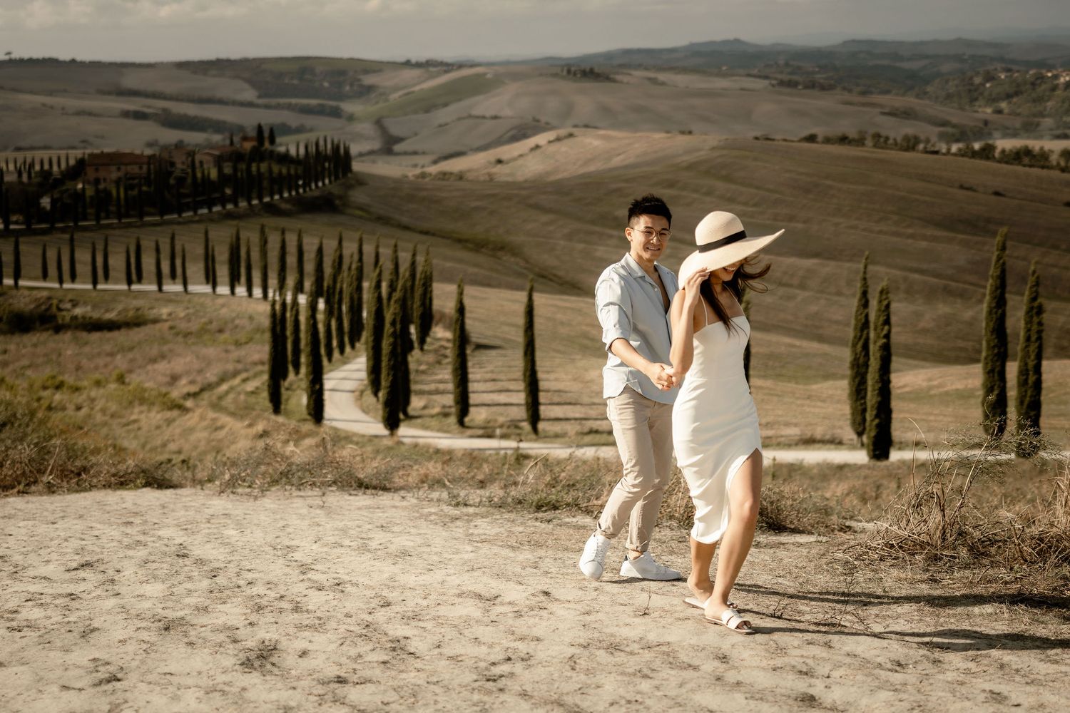 A romantic stroll along a cypress-lined path in Tuscany wearing coordinated white and beige outfits.