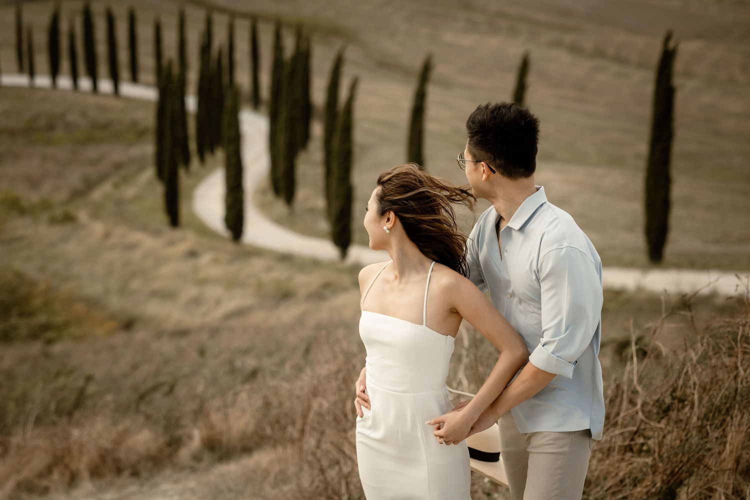 Couple in white clothing admiring scenic view with cypress trees in Tuscany countryside.
