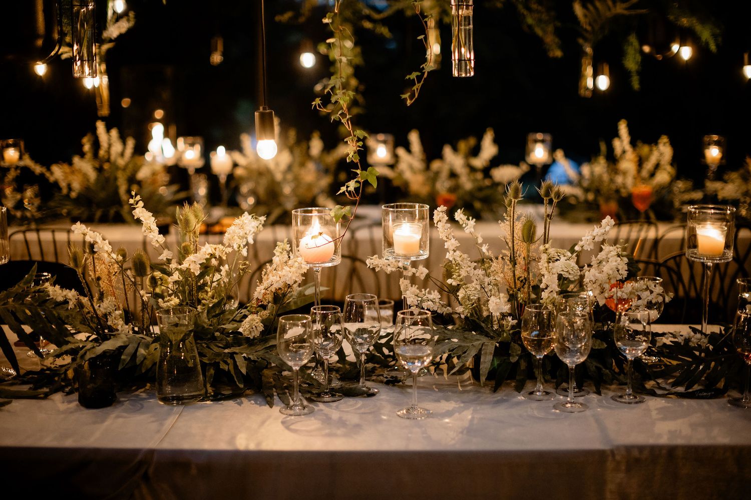 Elegant wedding table setting with hanging lights and natural floral decorations.