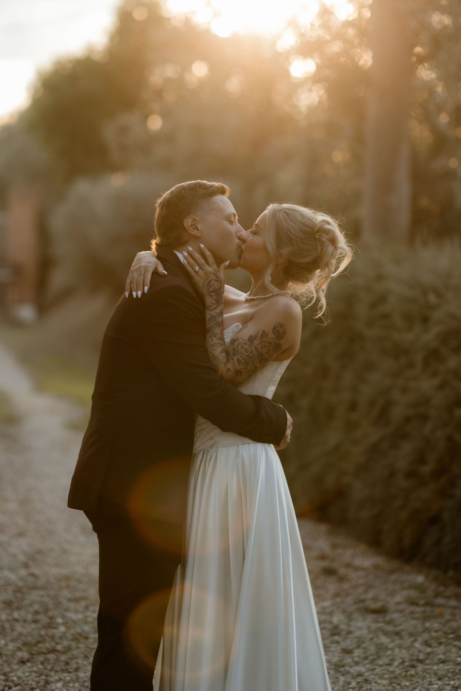 A romantic wedding couple shares a tender kiss at golden hour with sunlight creating dreamy bokeh in the background.