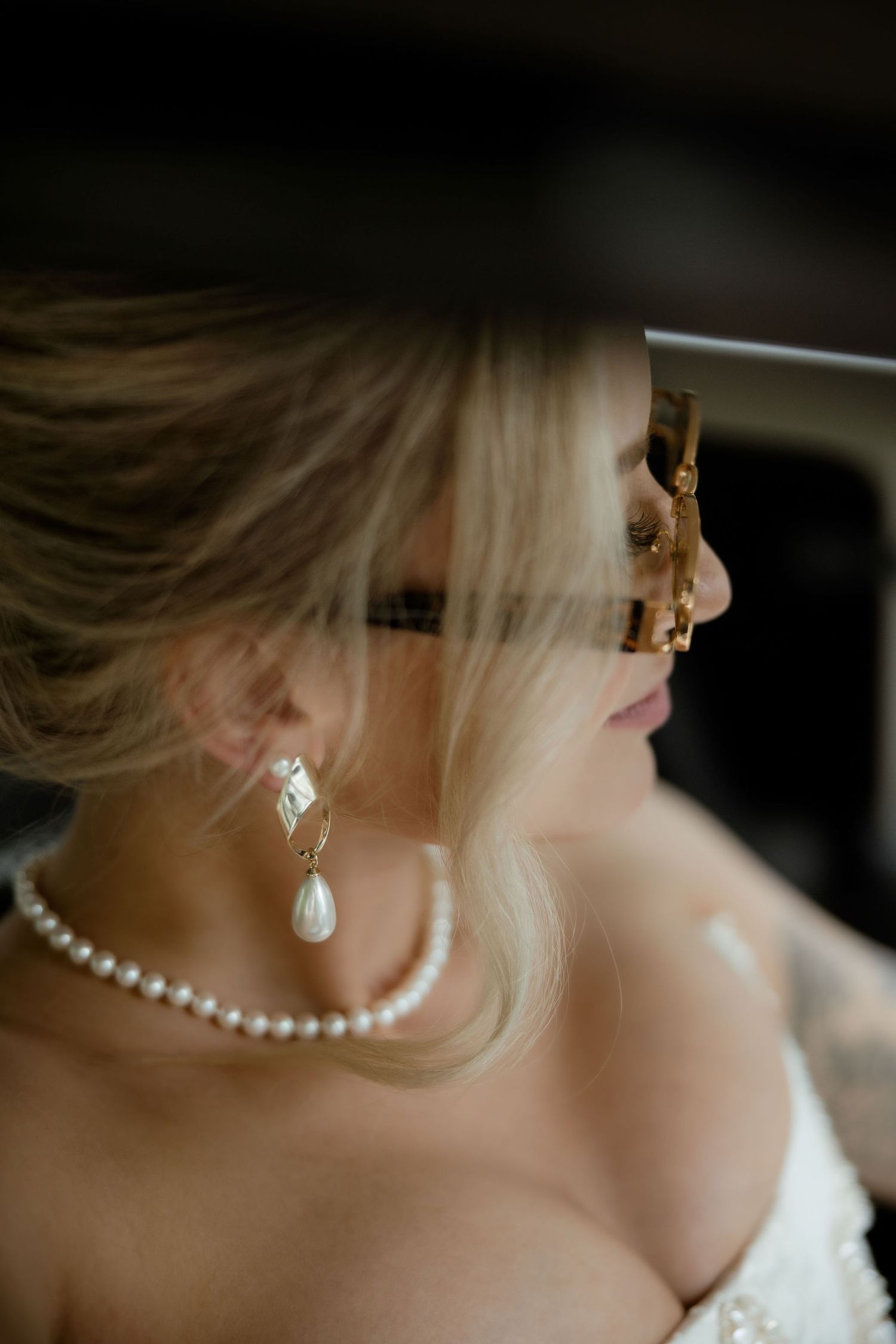 Close-up view of pearl jewelry and earrings on someone wearing a white dress in dramatic lighting.