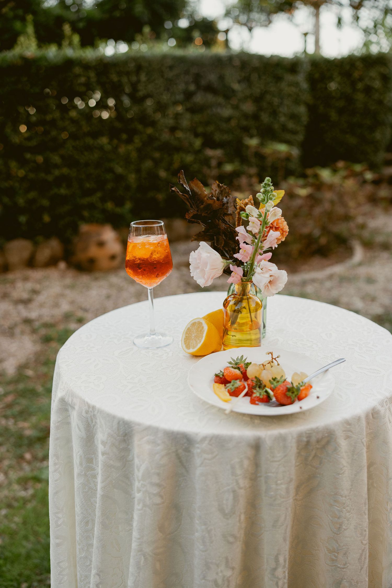 Elegant cocktail table settings with white tablecloths, floral arrangements, and amber-colored drinks in glassware at dusk.