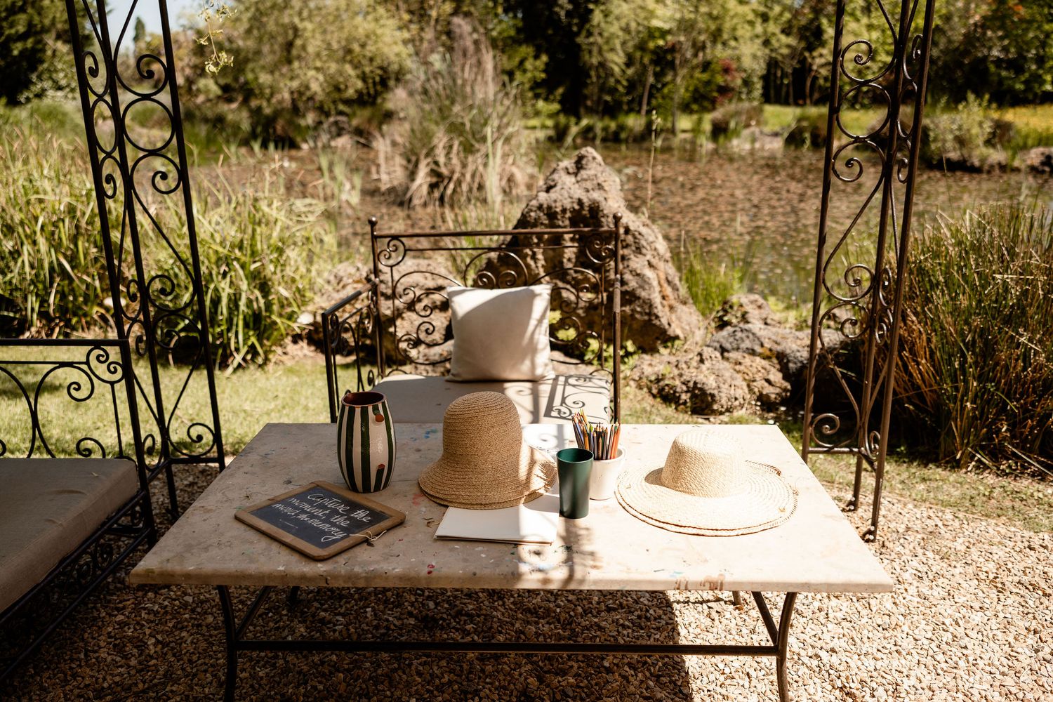 Rustic outdoor table setting with coffee and a straw hat on a garden porch swing in warm sunlight.