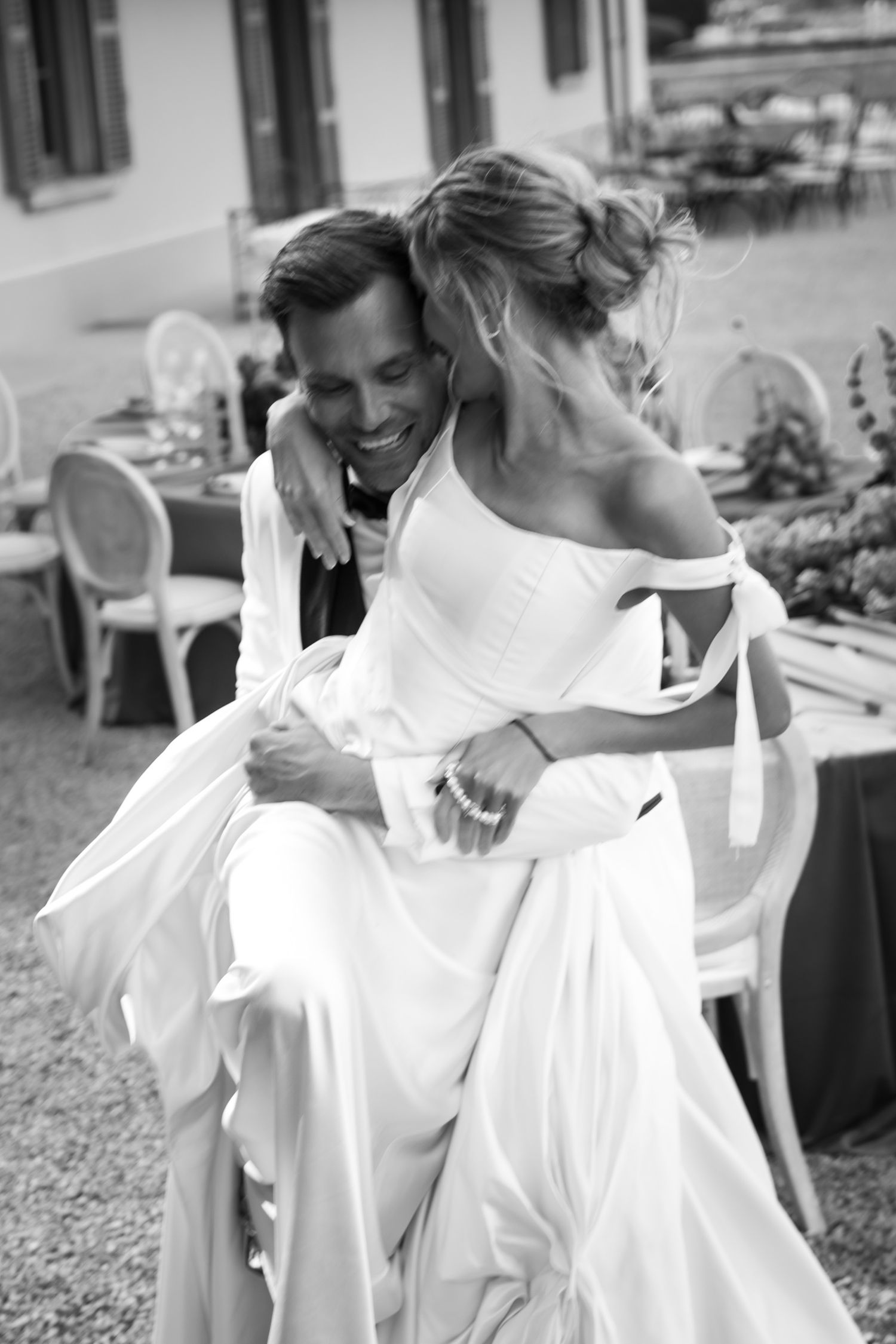 Black and white photo of groom carrying bride in elegant wedding dress outdoors at reception venue.