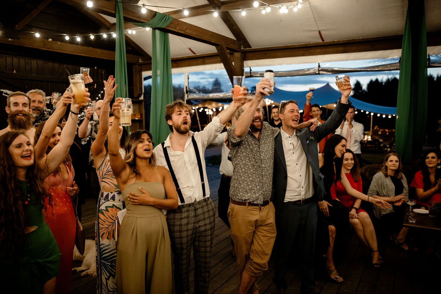 Wedding guests celebrate with raised arms on a festive dance floor at an evening reception party.