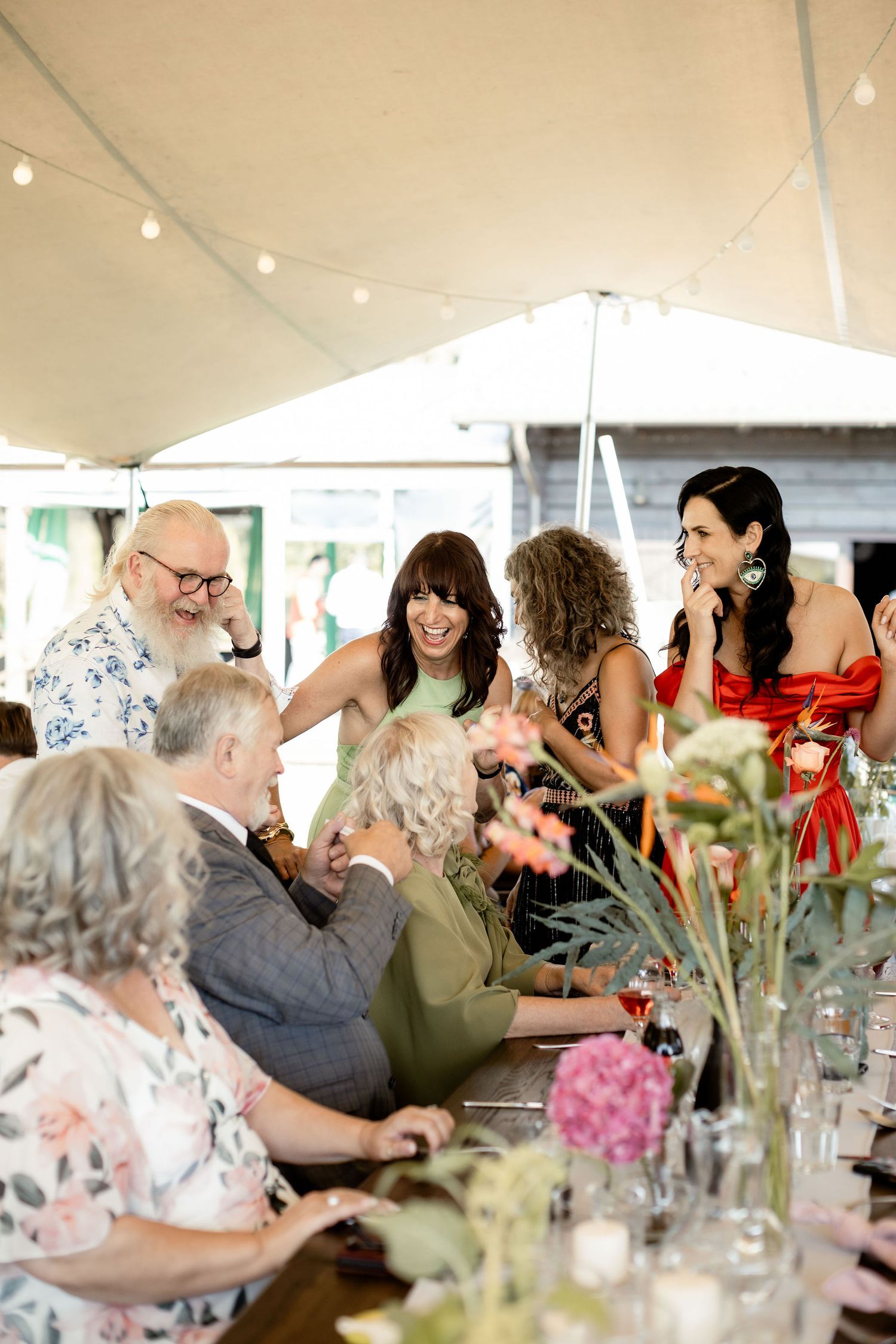 Outdoor wedding reception under a white tent with guests mingling around decorated tables.