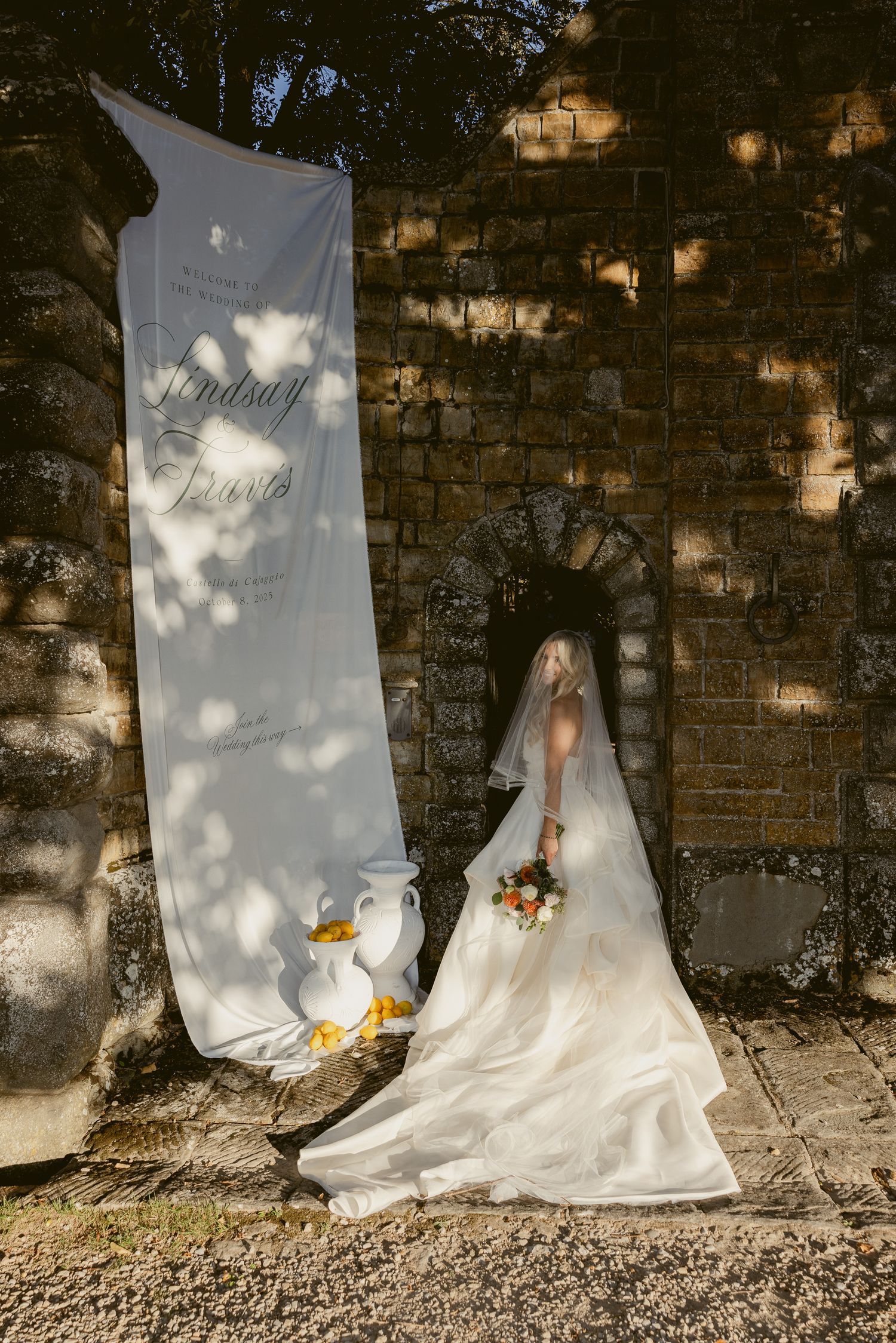 A white wedding dress photographed against a rustic brick wall with dappled sunlight creating a dreamy atmosphere.