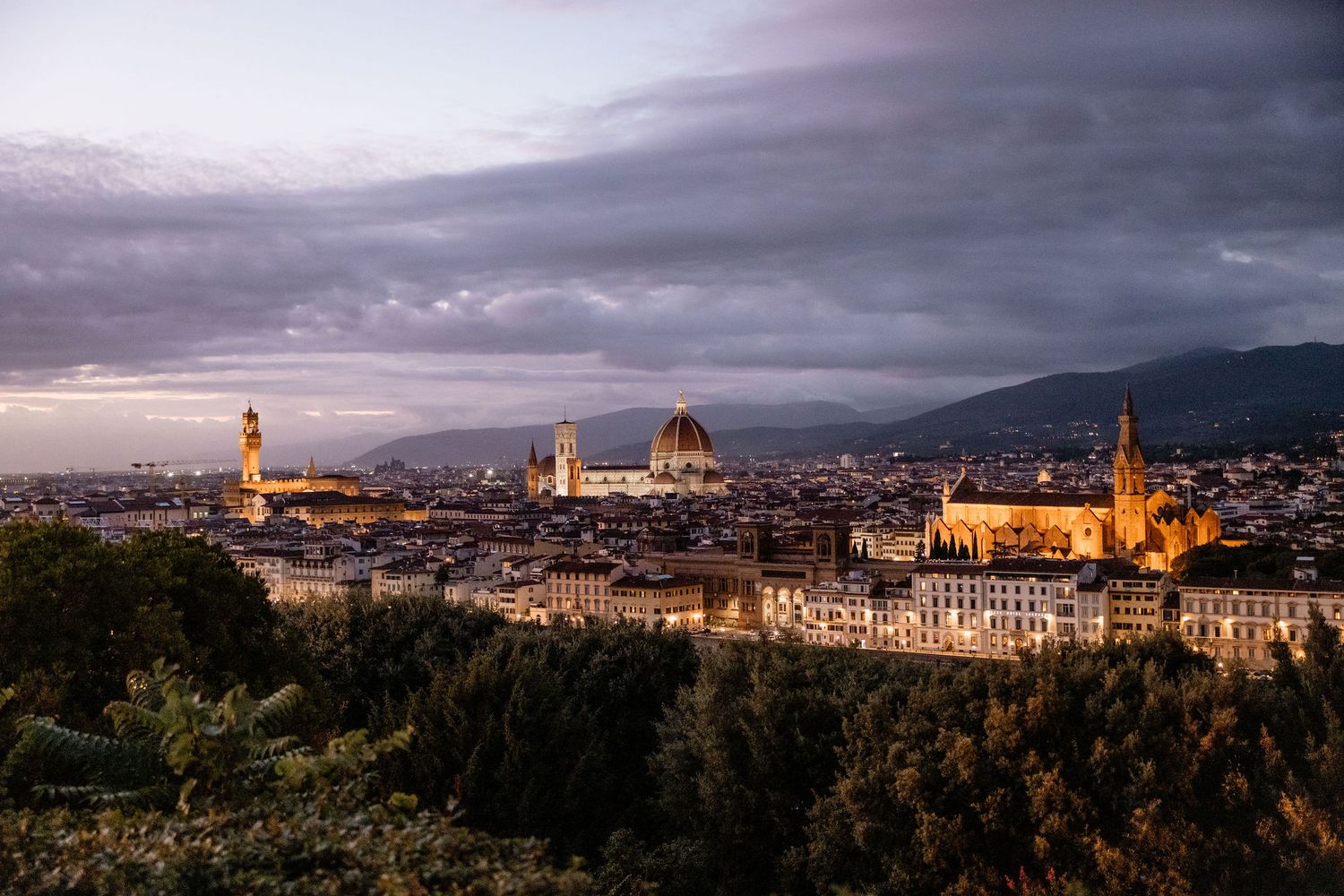Stunning sunset view of Florence's historic skyline with golden light illuminating the Duomo and Palazzo Vecchio tower.