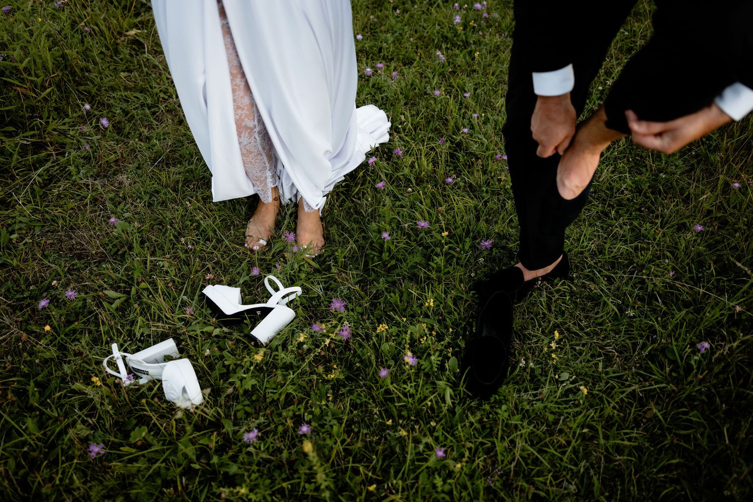 Close-up view of feet on grass with discarded white shoes, contrasting black and white formal attire visible.