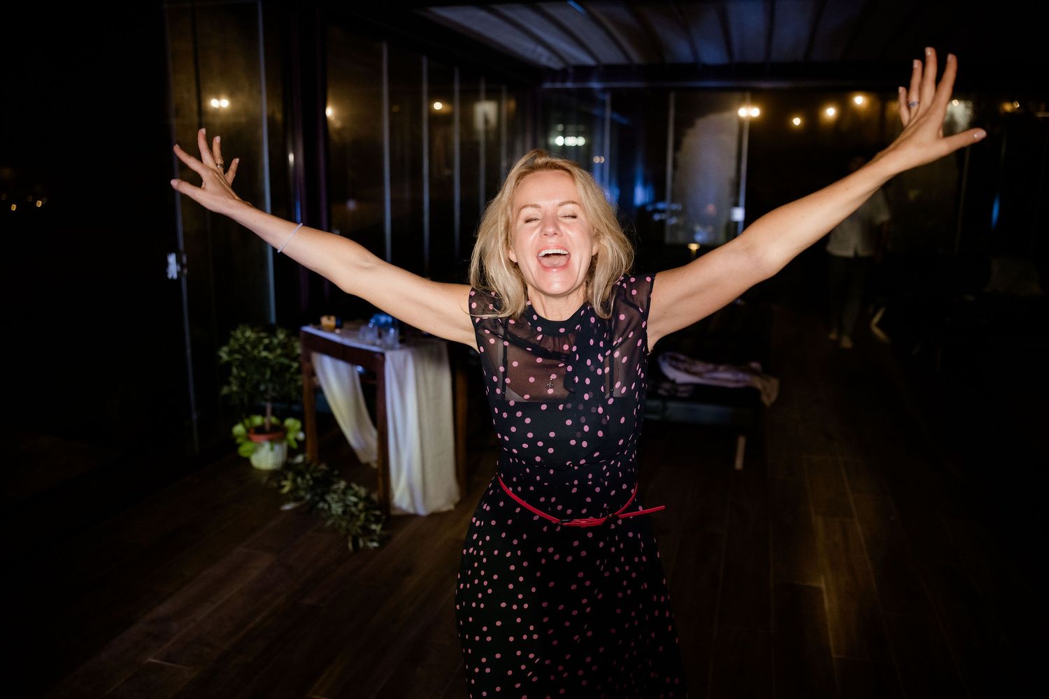 Person dancing with arms raised in celebration at a nighttime party venue with string lights visible overhead.