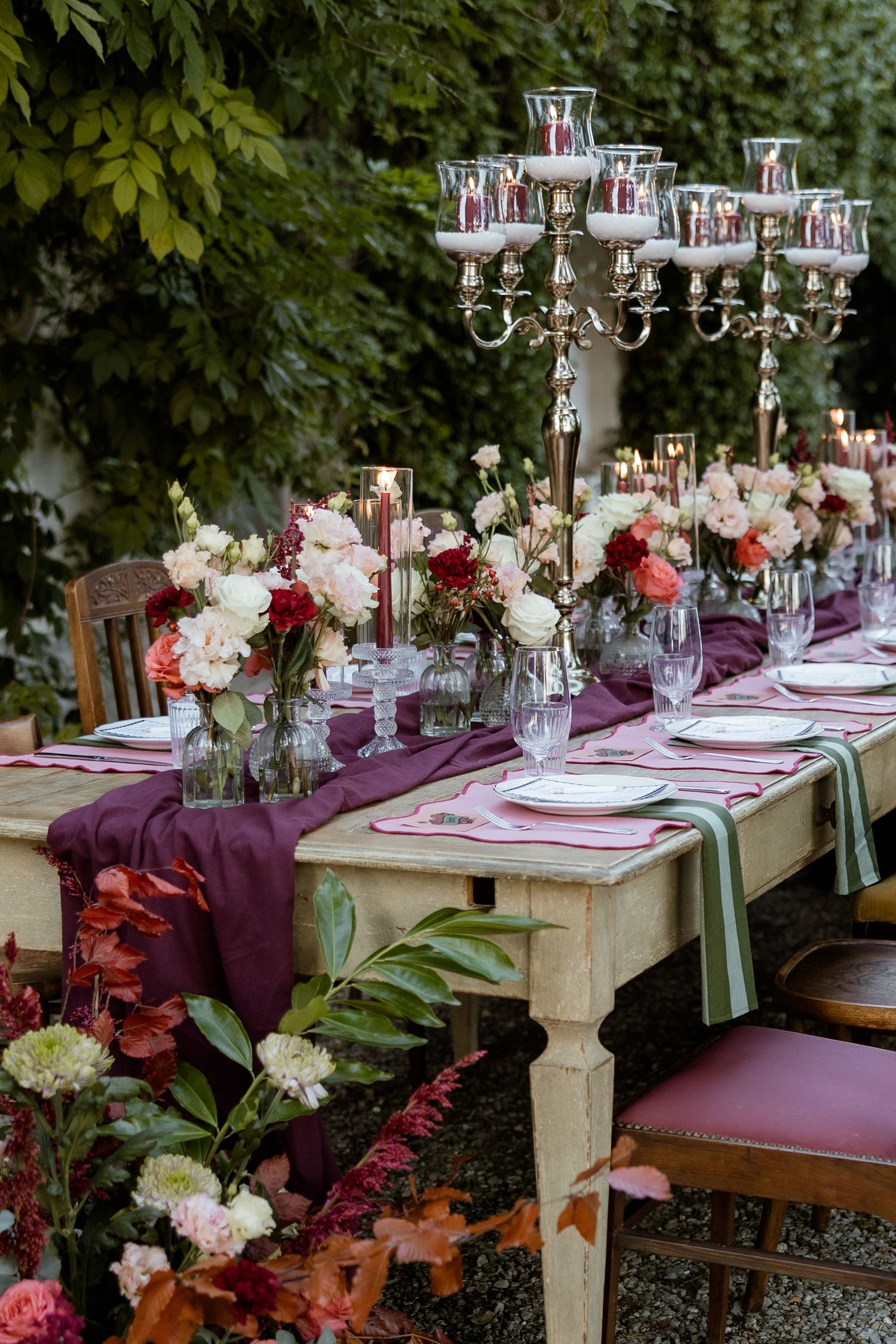 Elegant outdoor dining table set with purple linens, crystal candelabras, and floral arrangements in a garden setting.