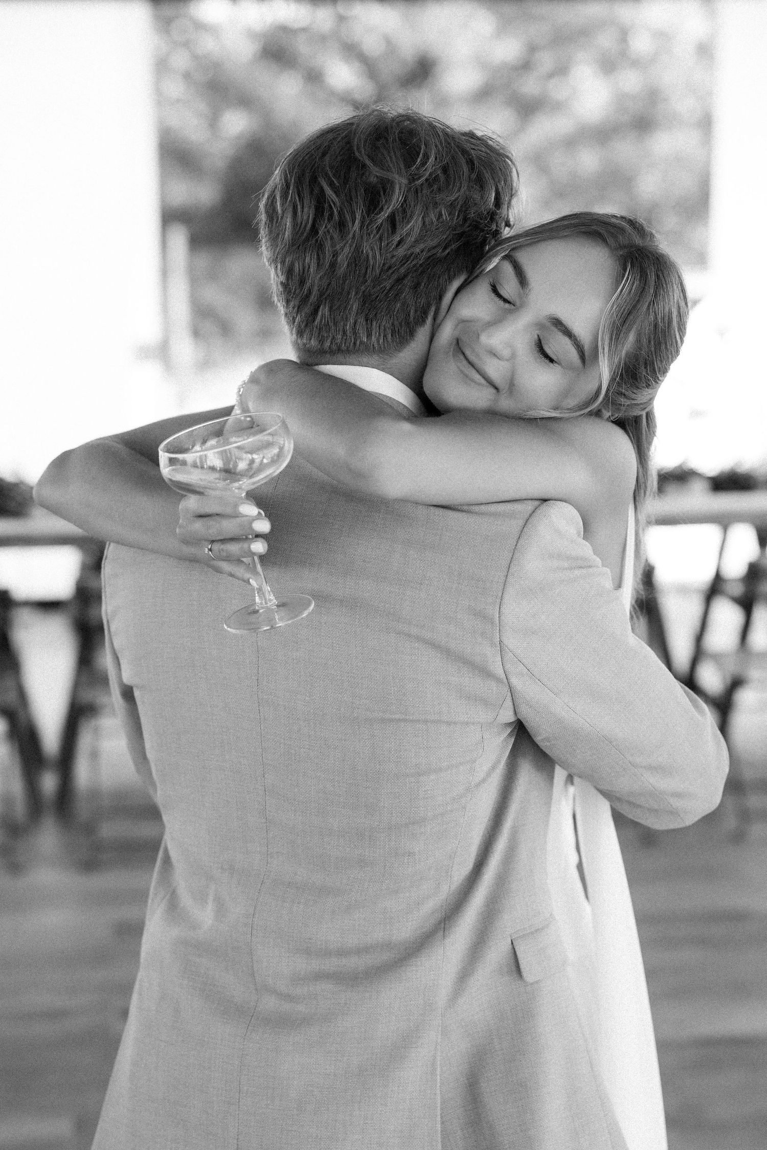 A tender black and white photo of a couple embracing on a dance floor while one holds a champagne glass.