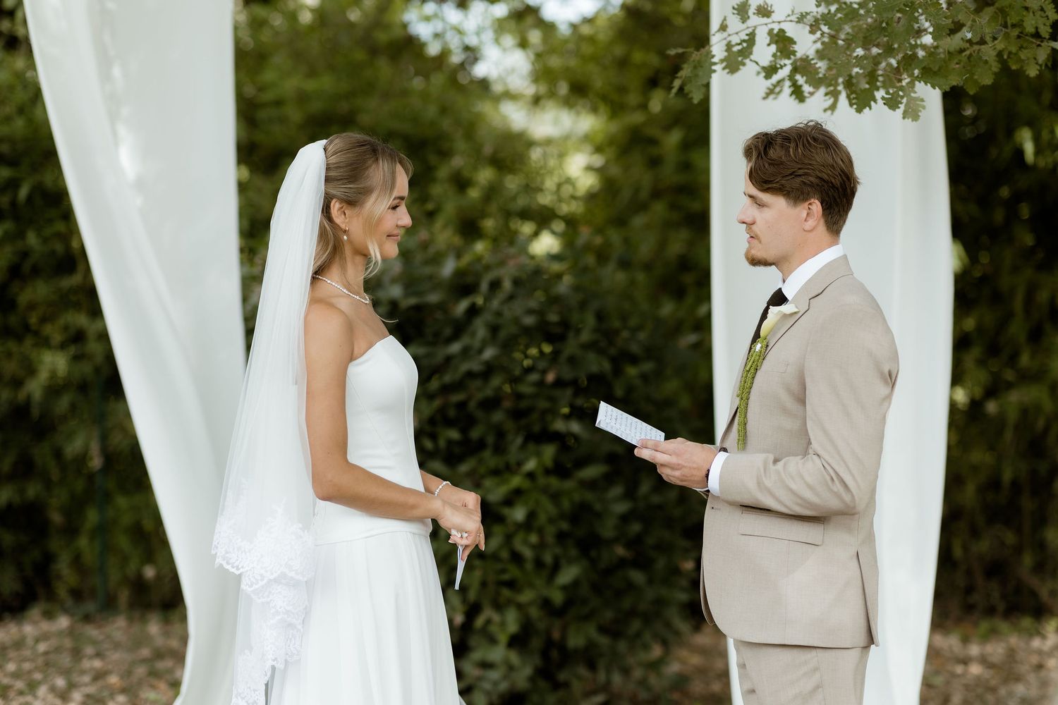 A couple shares tender moments during their outdoor wedding ceremony with flowing white curtains and greenery.