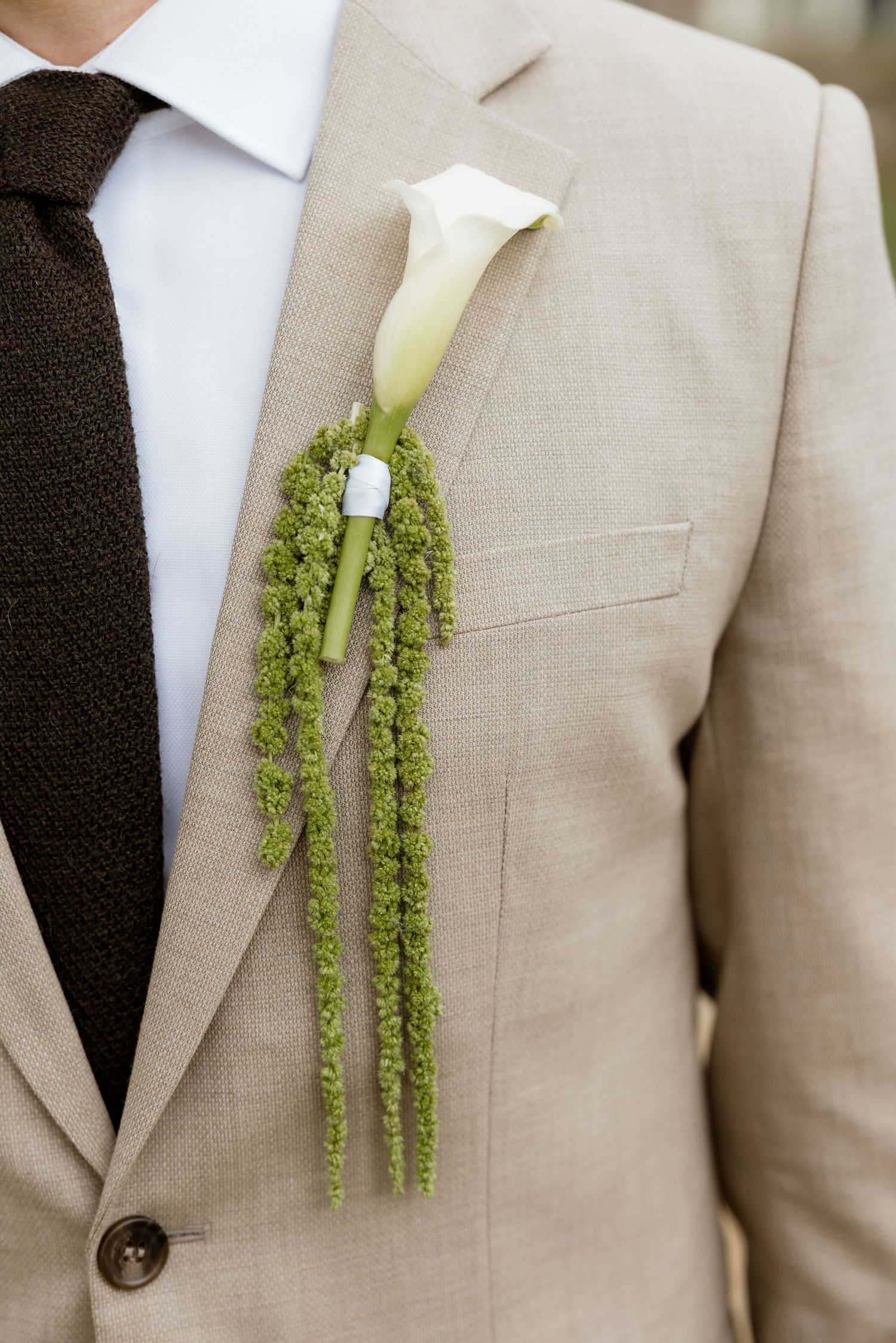 A series of elegant white calla lily boutonnieres with cascading green amaranthus on tan suit lapels.