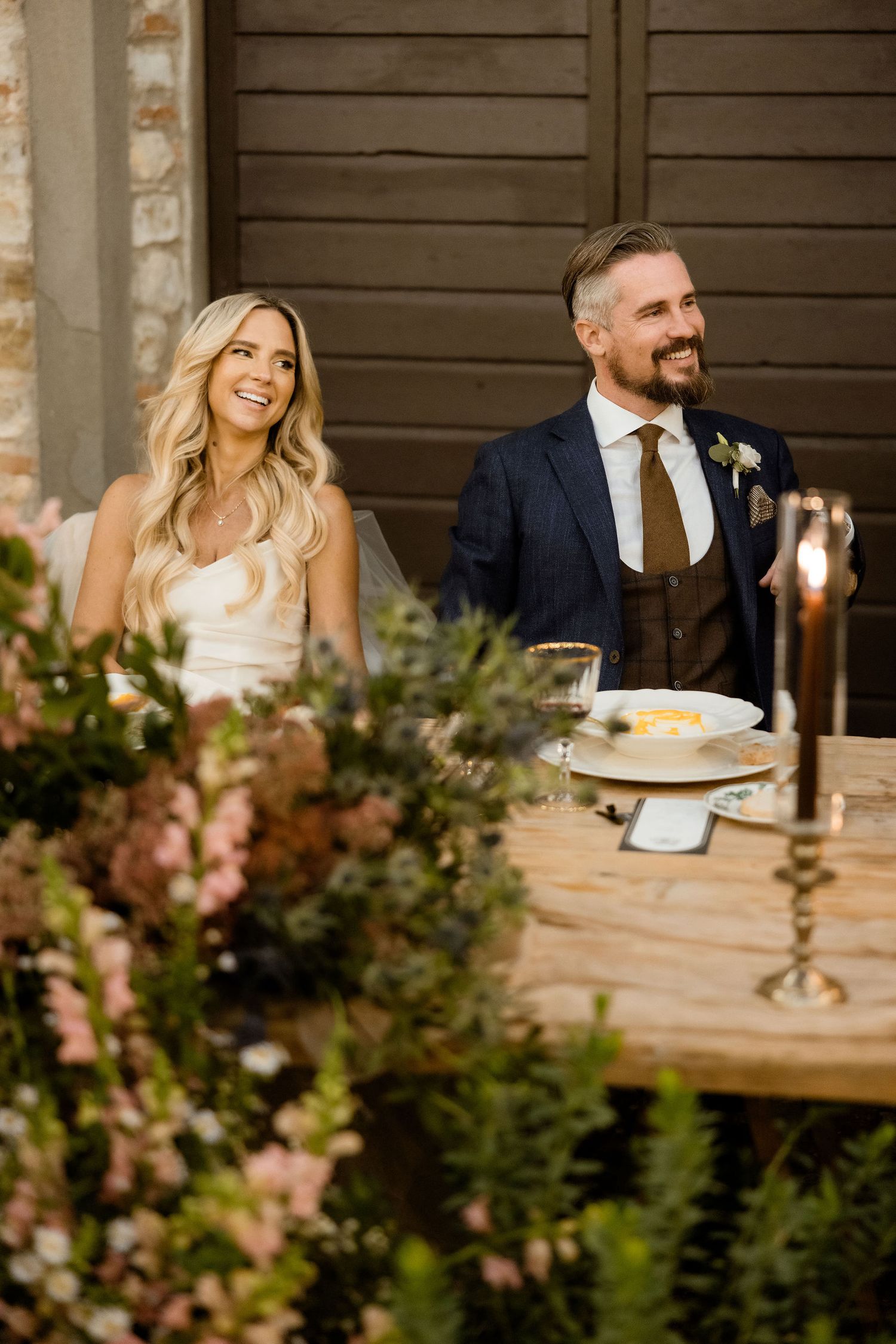 A couple shares a joyful moment at their rustic outdoor wedding reception with greenery and candlelight decor.