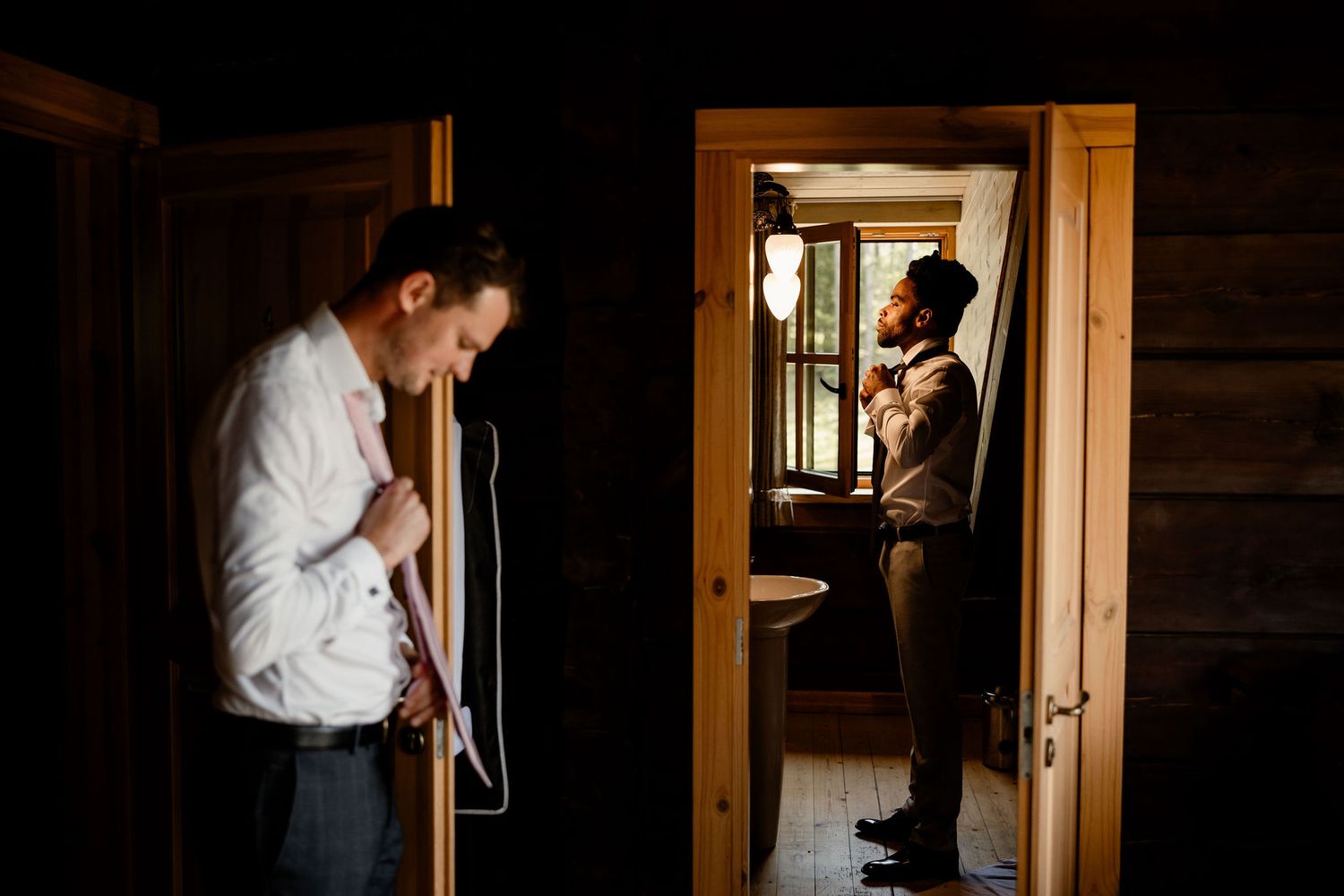 Two people in white shirts prepare in a dimly lit rustic room with wooden details.