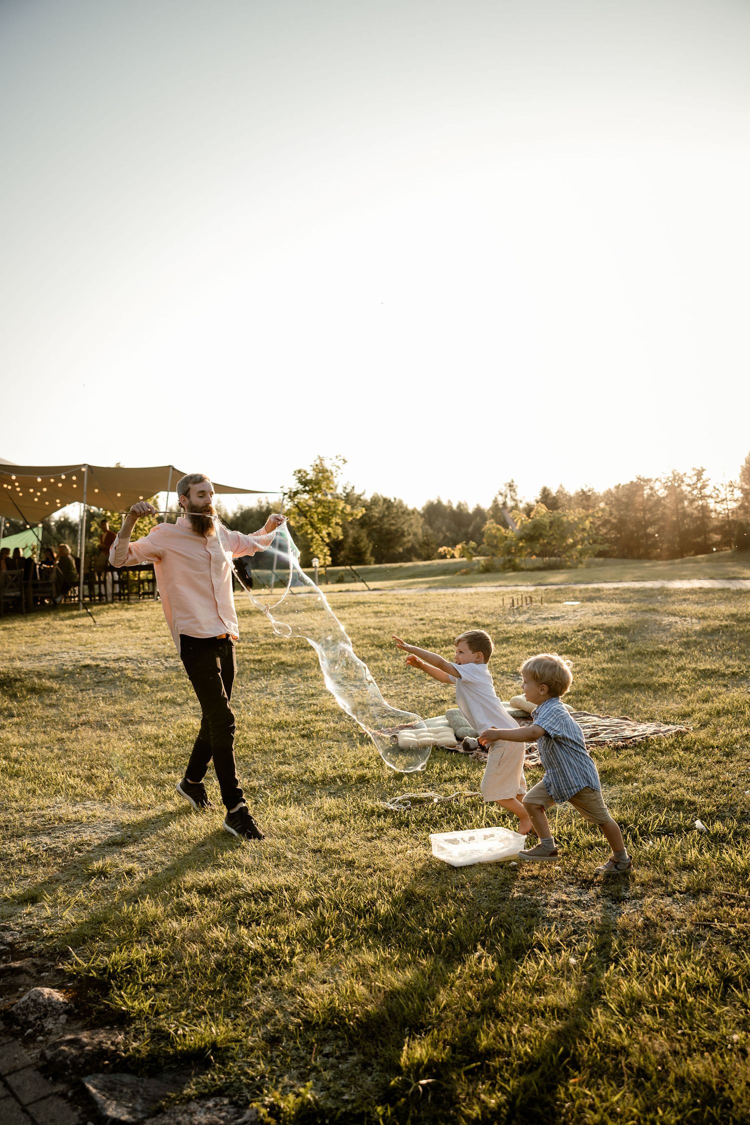 Children playing with bubbles at outdoor wedding reception during golden hour.
