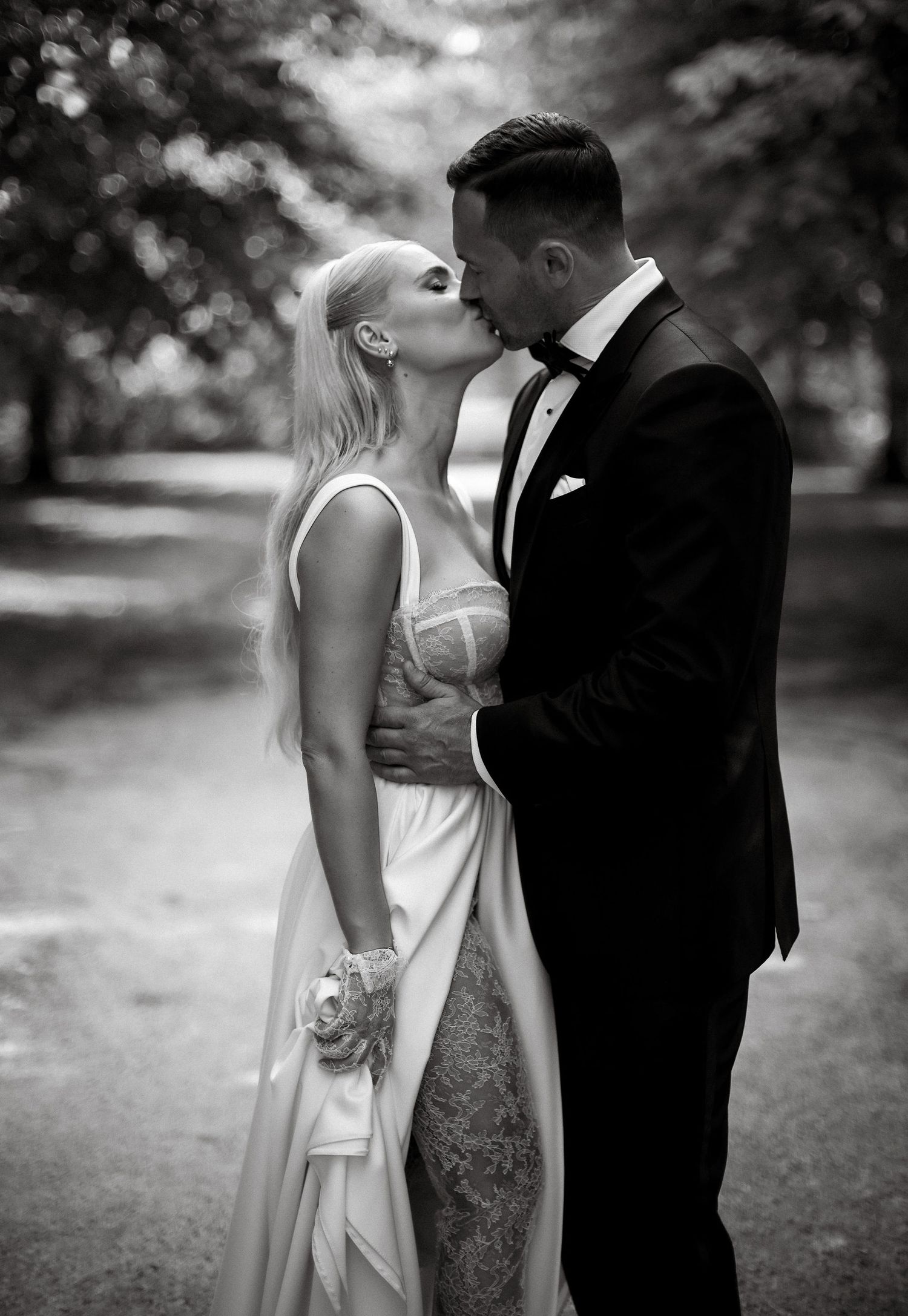 Intimate black and white wedding portrait showing a tender kiss in a garden setting.