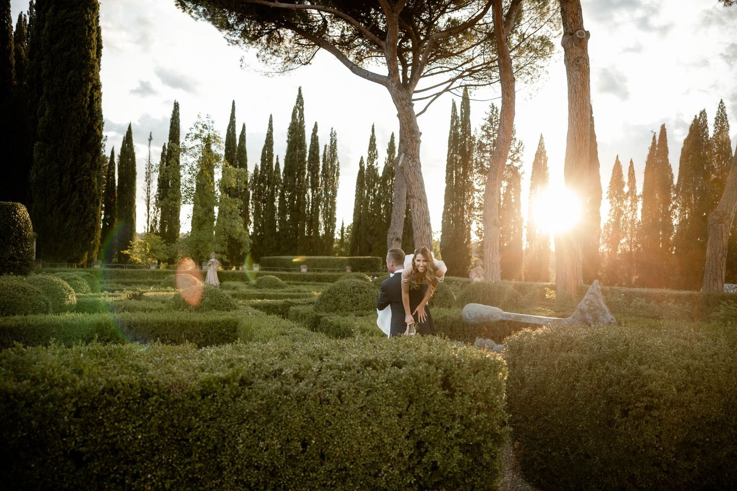 Golden sunset light streams through cypress trees in romantic Italian garden setting.