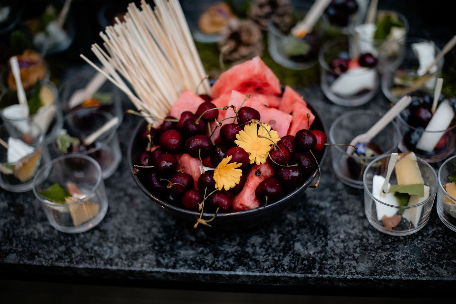 Beautiful maroon and orange flower petals in a dark bowl with wooden cocktail sticks arranged on a black surface.