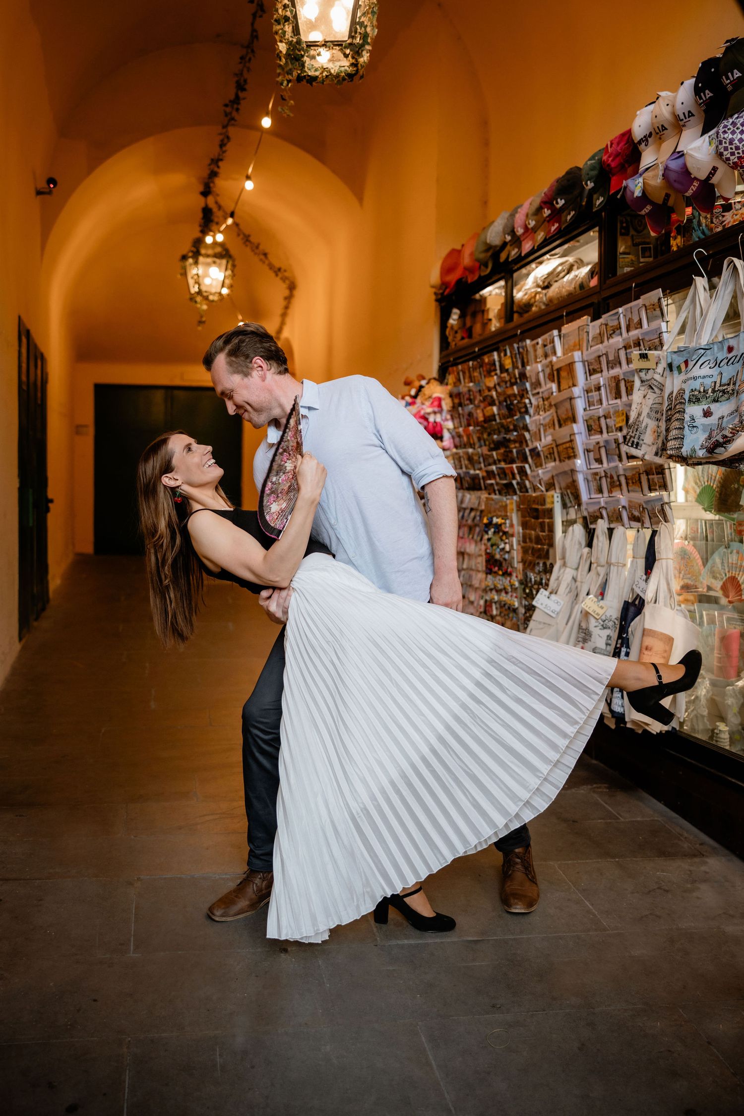 A romantic dance dip between a couple in an arched hallway with lanterns and a rustic brick wall.