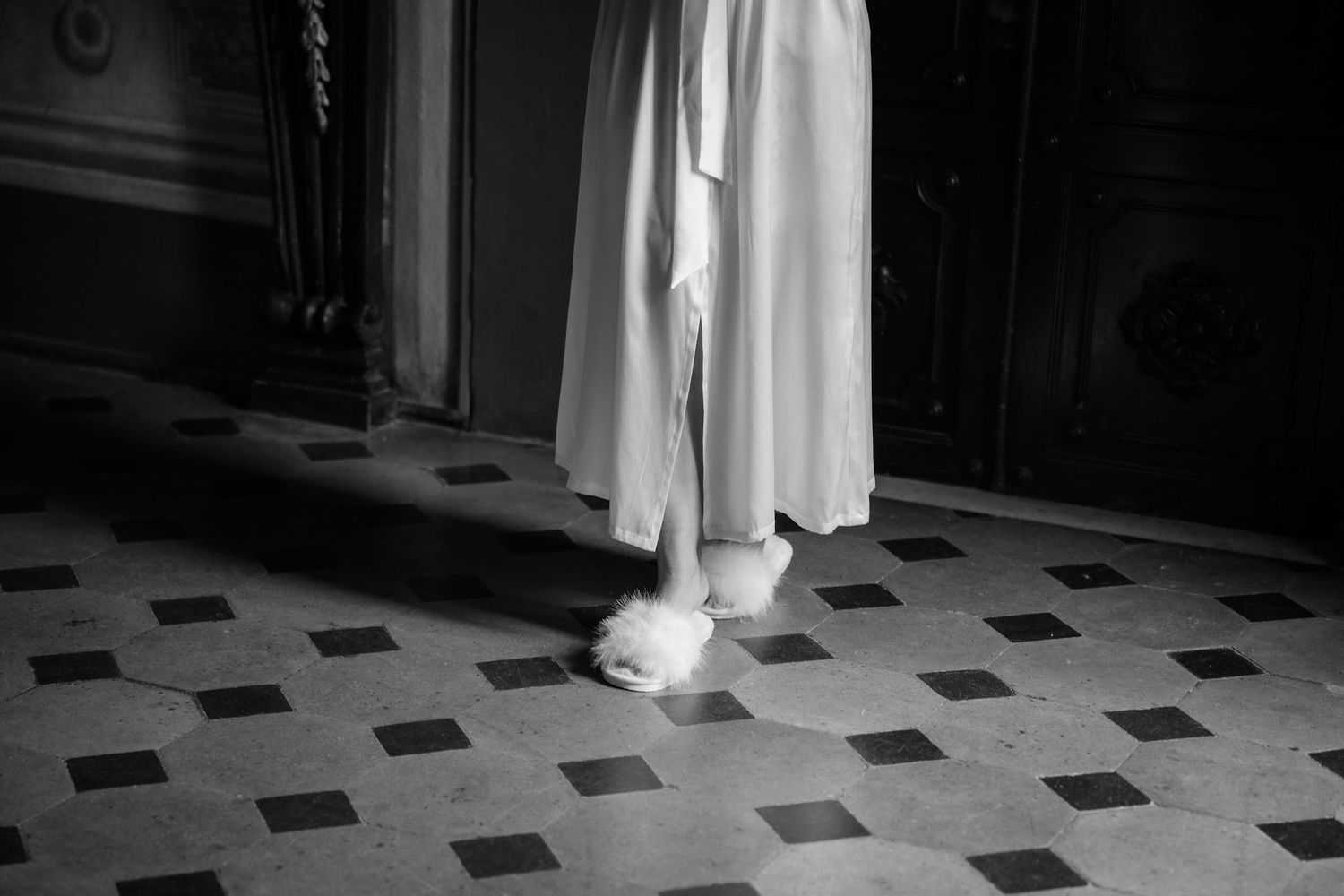 A black and white photograph shows white robes and slippers on a geometric tiled floor.