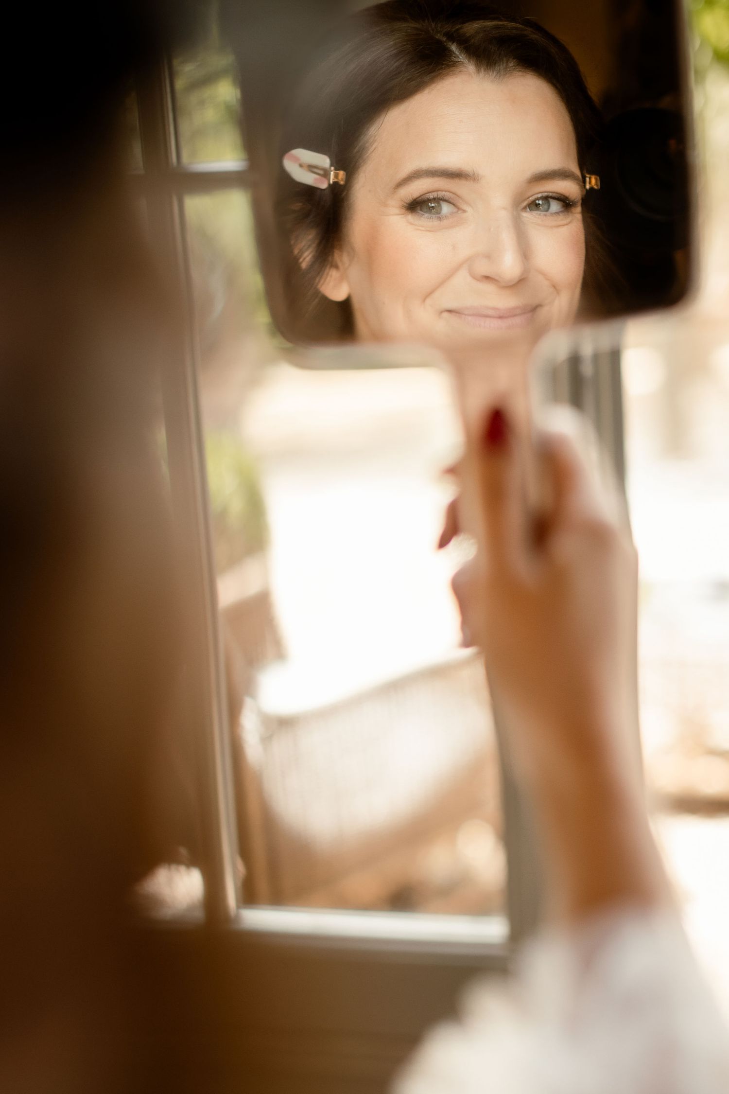 Reflection in mirror shows preparations for a wedding with soft lighting and makeup application.