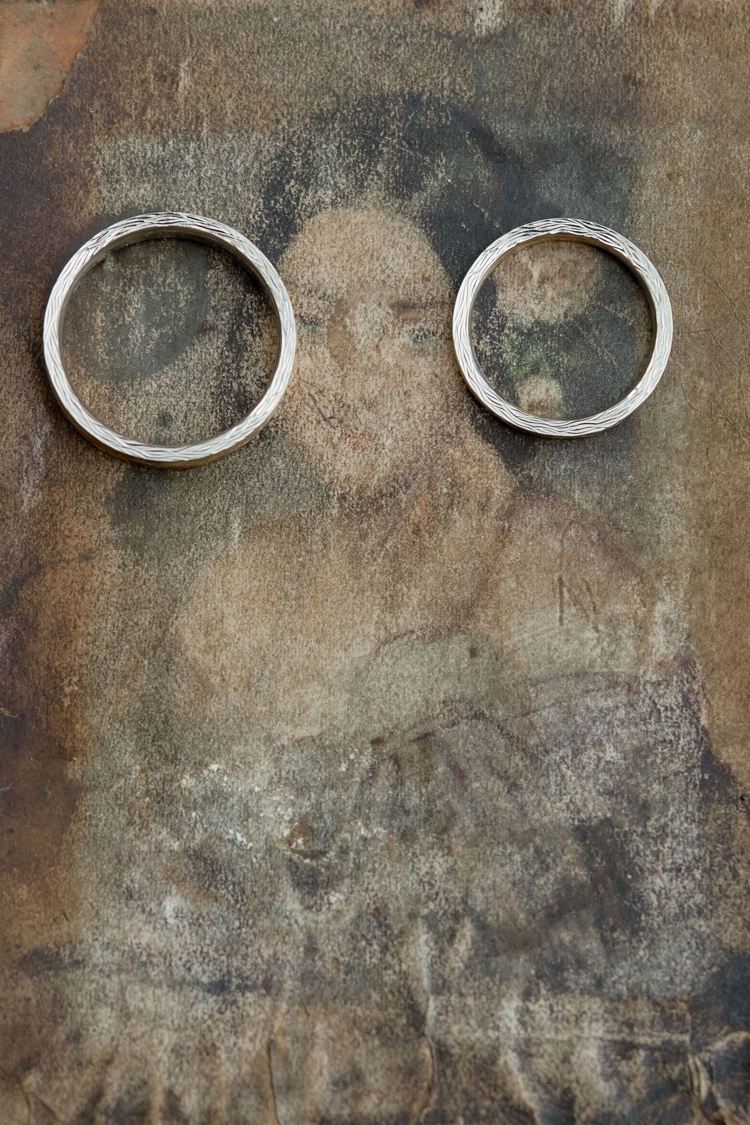 Two silver wedding rings placed on a weathered gray textured background with a vintage patina effect.