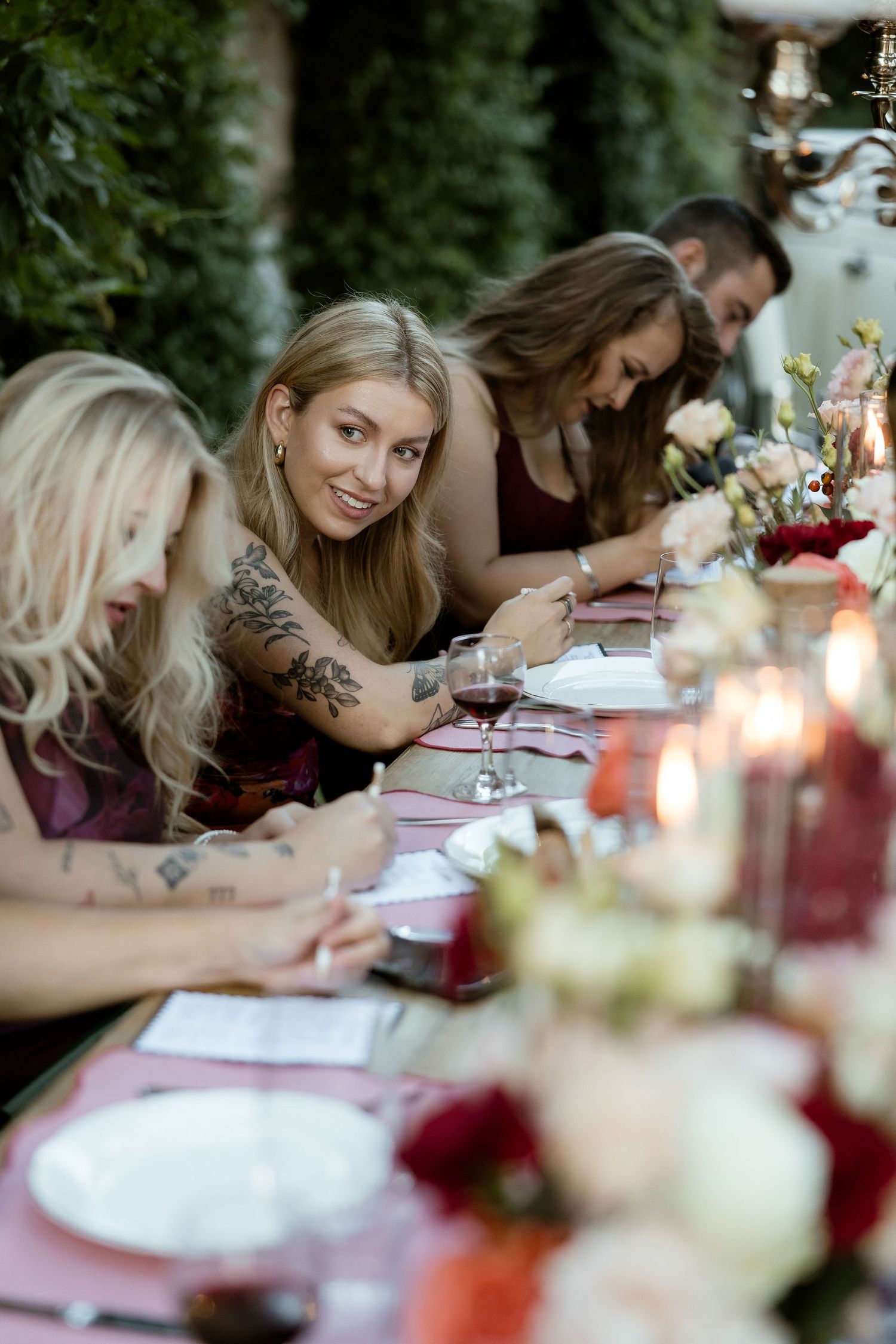 Wedding guests write messages and well-wishes at an elegant outdoor reception table with candlelight and floral decor.