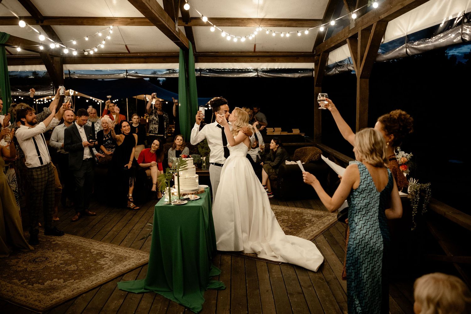Wedding guests celebrate and take photos during a festive reception at a rustic wooden venue with ceiling beams.