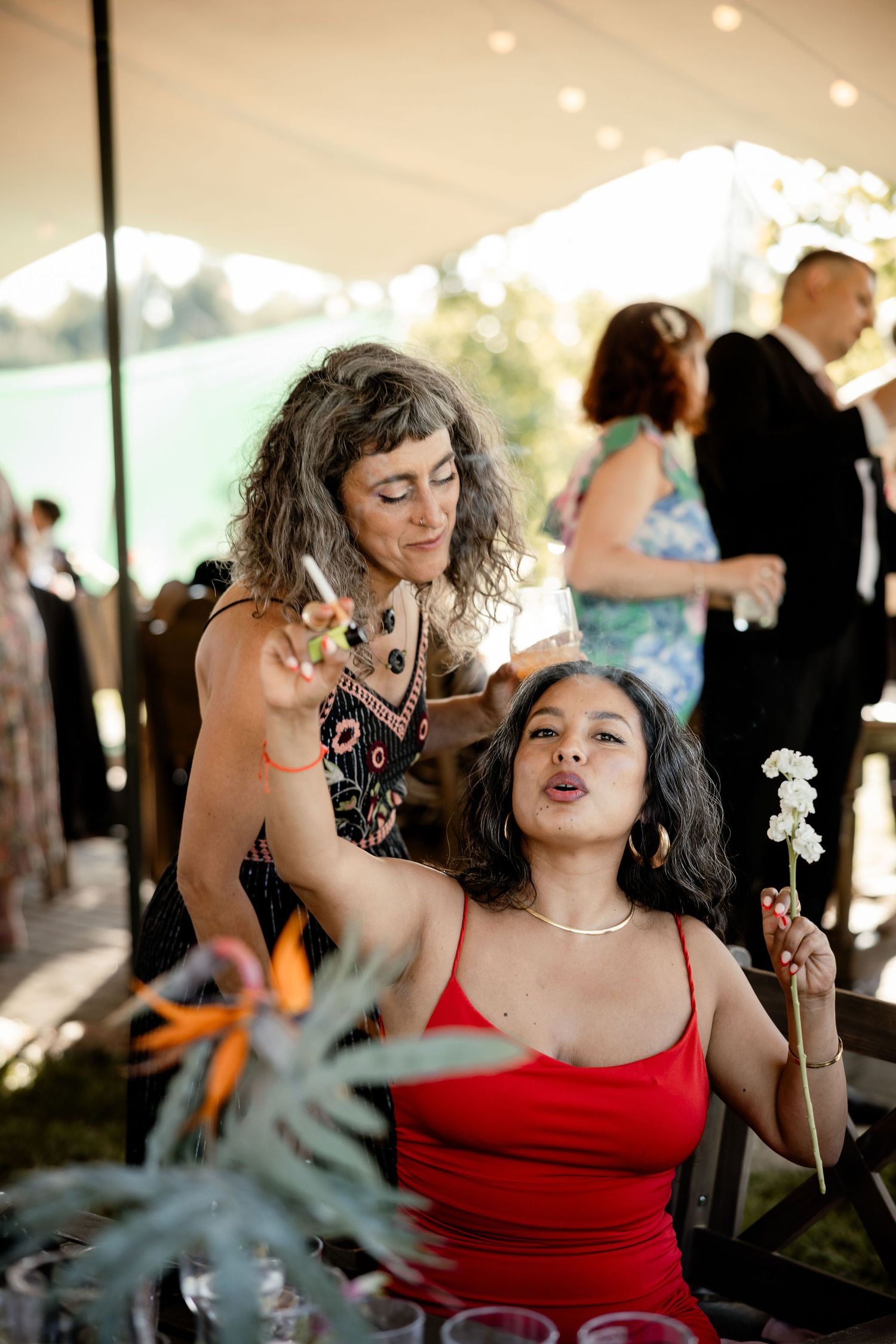 Two guests enjoying a playful moment with a dandelion at an outdoor wedding reception.