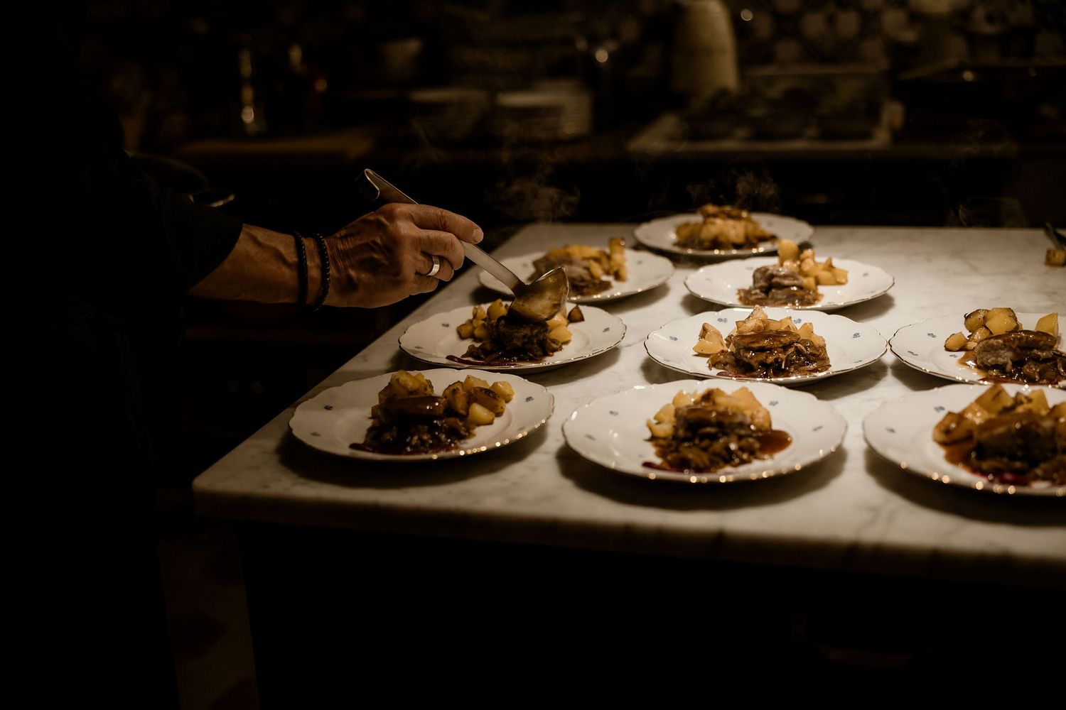 Multiple plates of gourmet food arranged on a dark wooden surface in moody restaurant lighting.