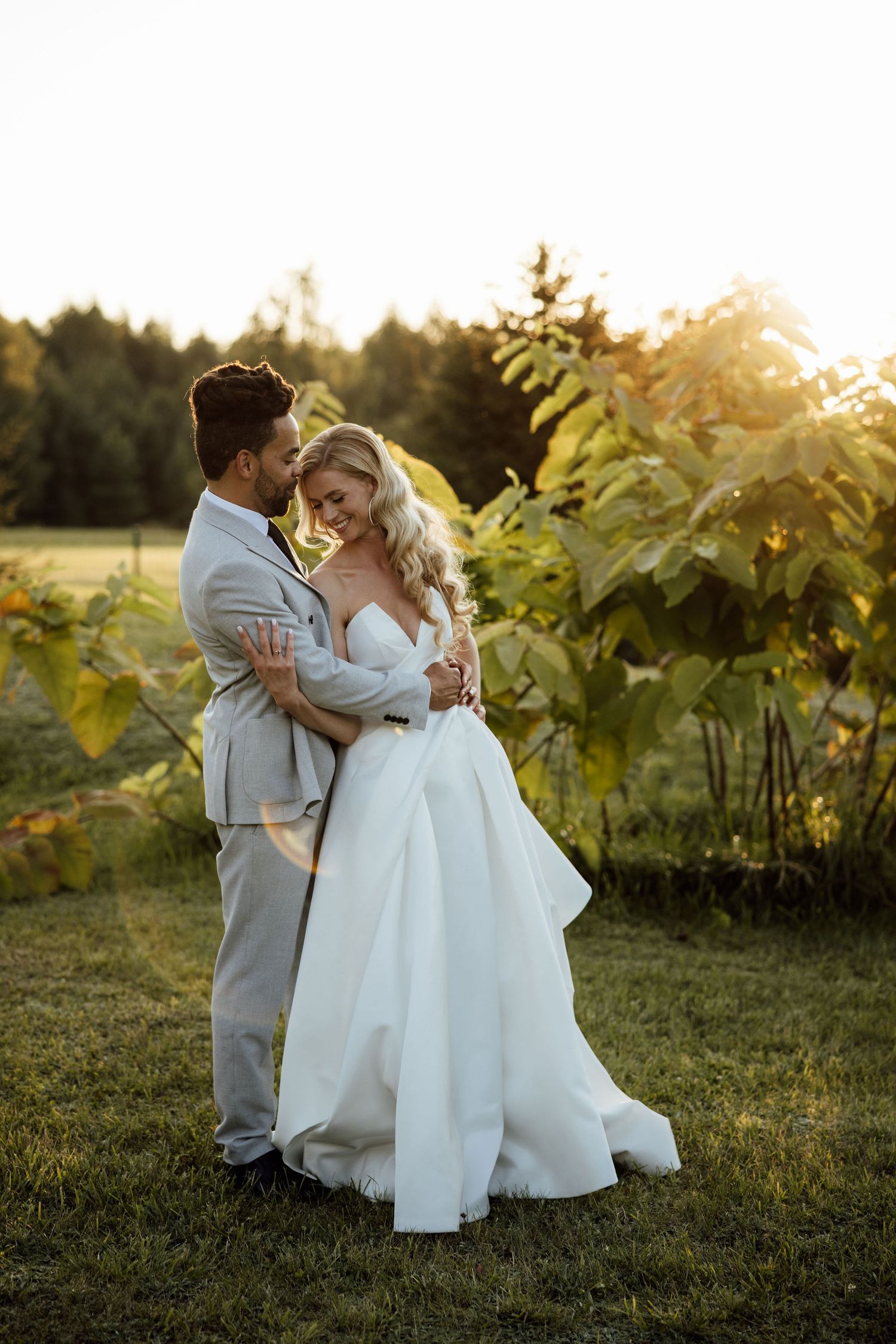 A romantic couple embraces in a vineyard at golden hour during their wedding photoshoot.