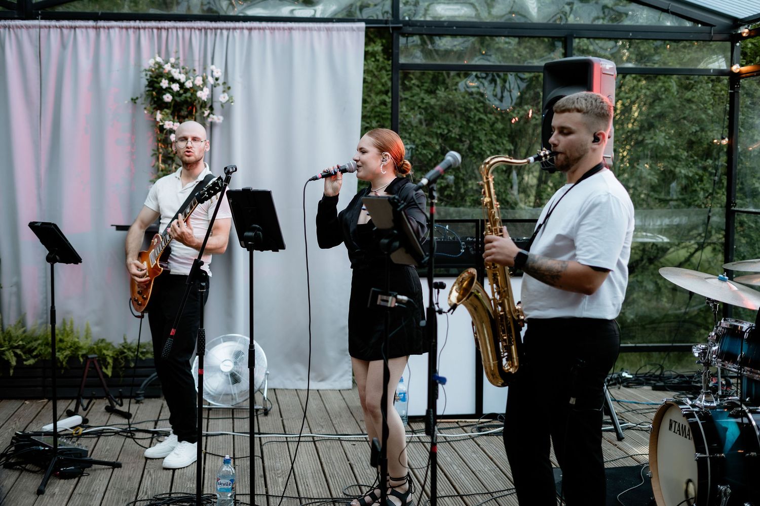 Live band performing at a wedding reception with guitar, vocals and saxophone on an outdoor deck.